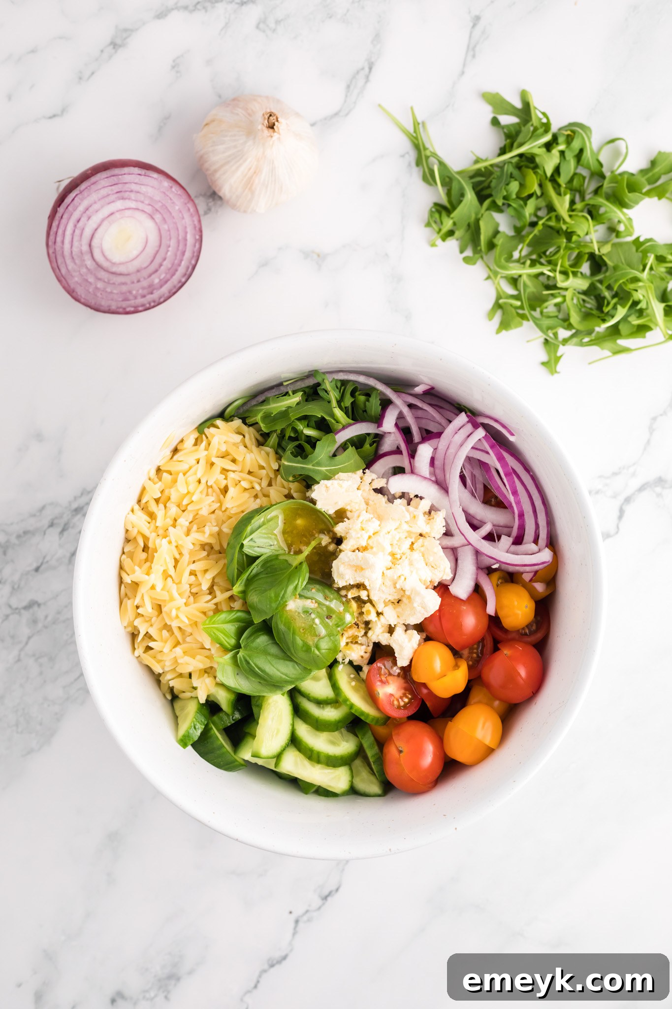 All the fresh ingredients for Arugula Orzo Salad gathered in a large mixing bowl before dressing.