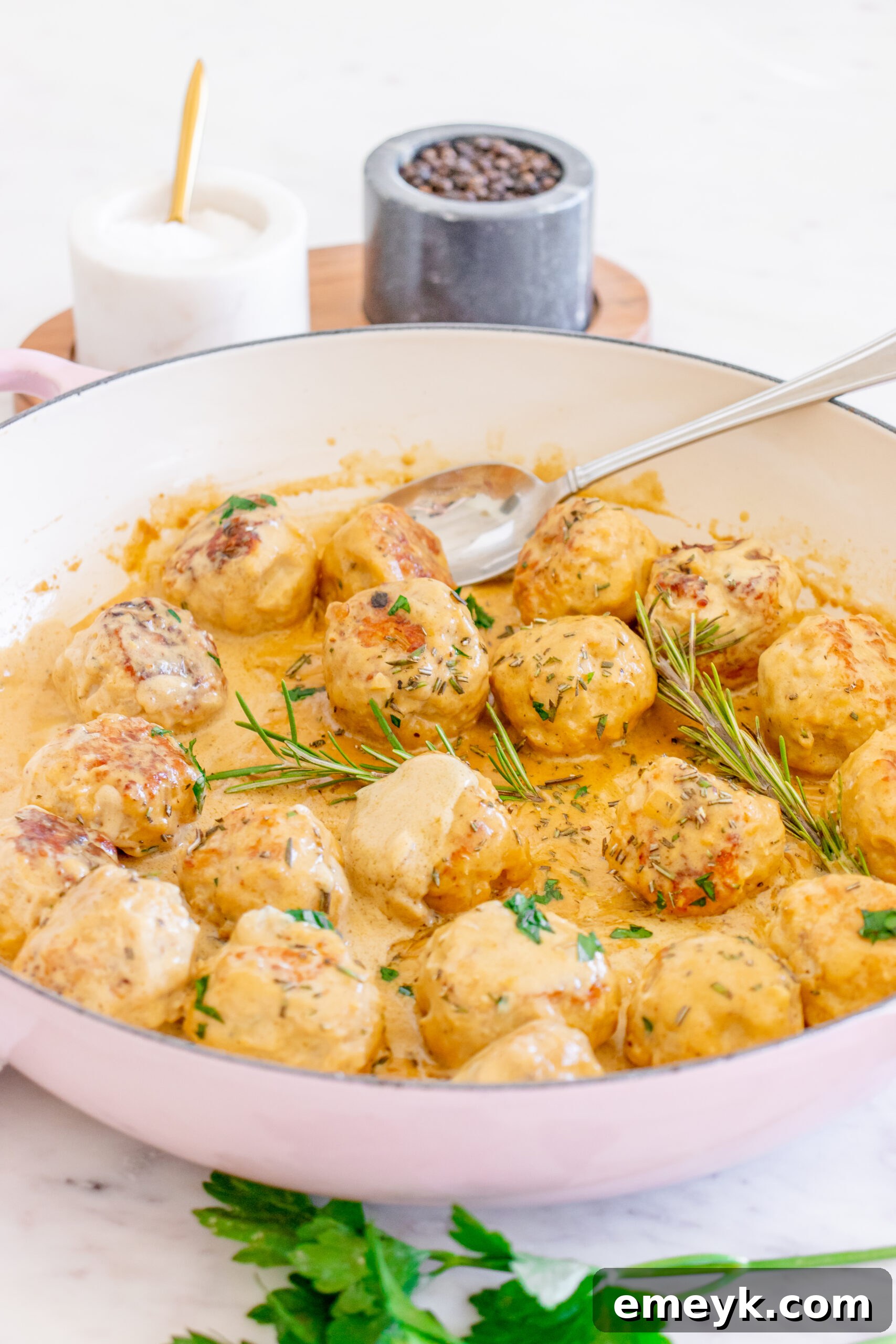 A pot of golden brown Maple Dijon Turkey Meatballs swimming in a rich, creamy sauce, garnished with fresh herbs.