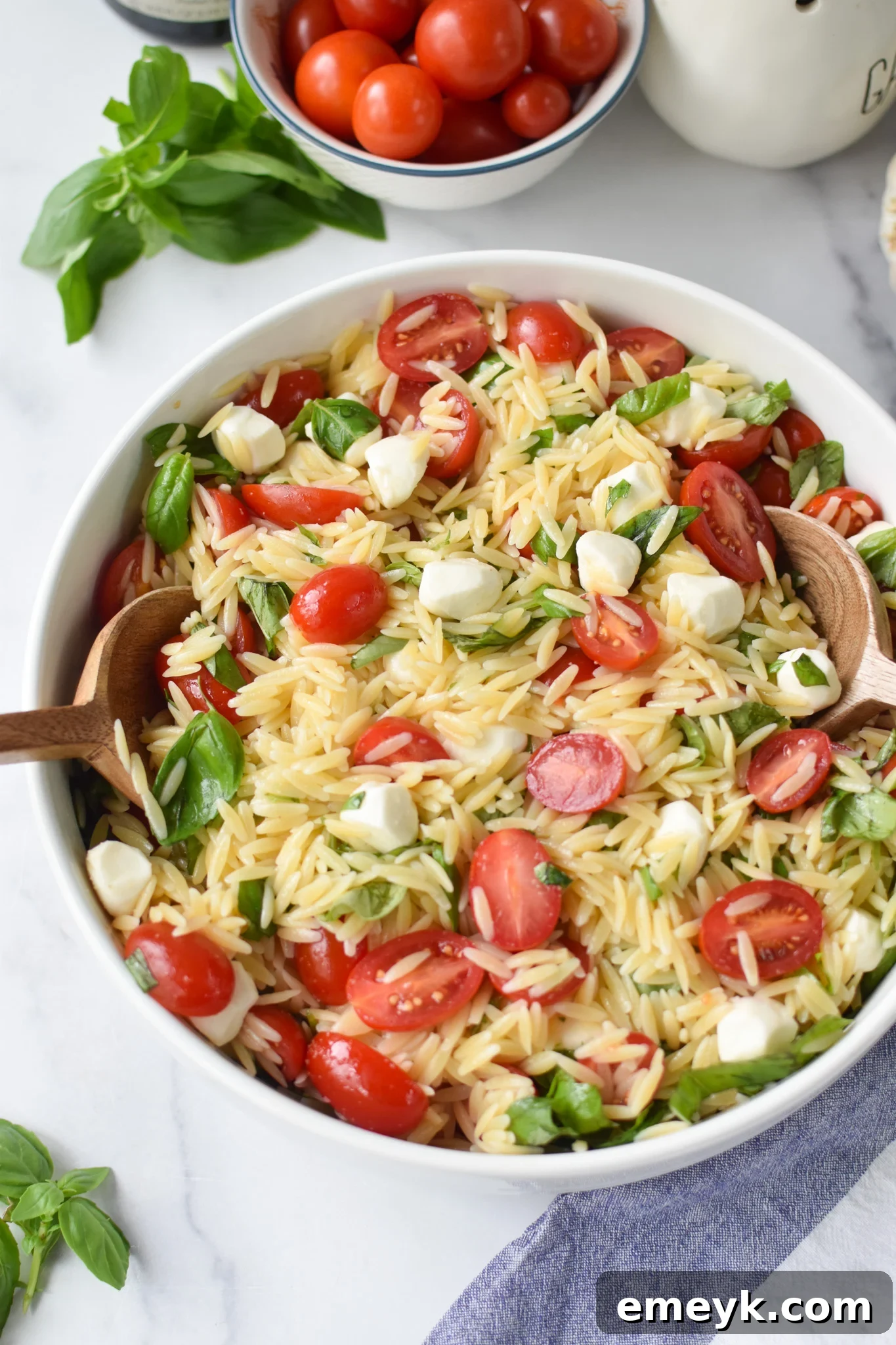 Caprese Orzo Delight 3 Serving Caprese Orzo Pasta Salad with wooden spoons in a rustic bowl.