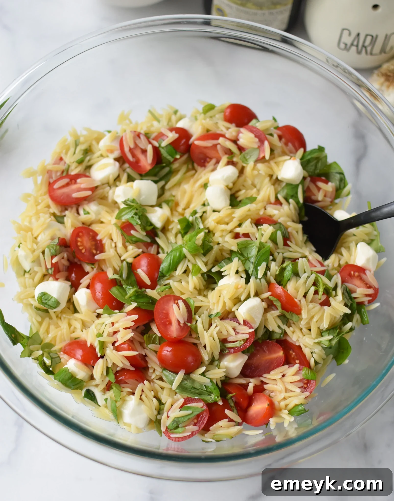 Caprese Orzo Delight 9 Caprese Orzo Pasta Salad being tossed with balsamic dressing in a glass bowl.