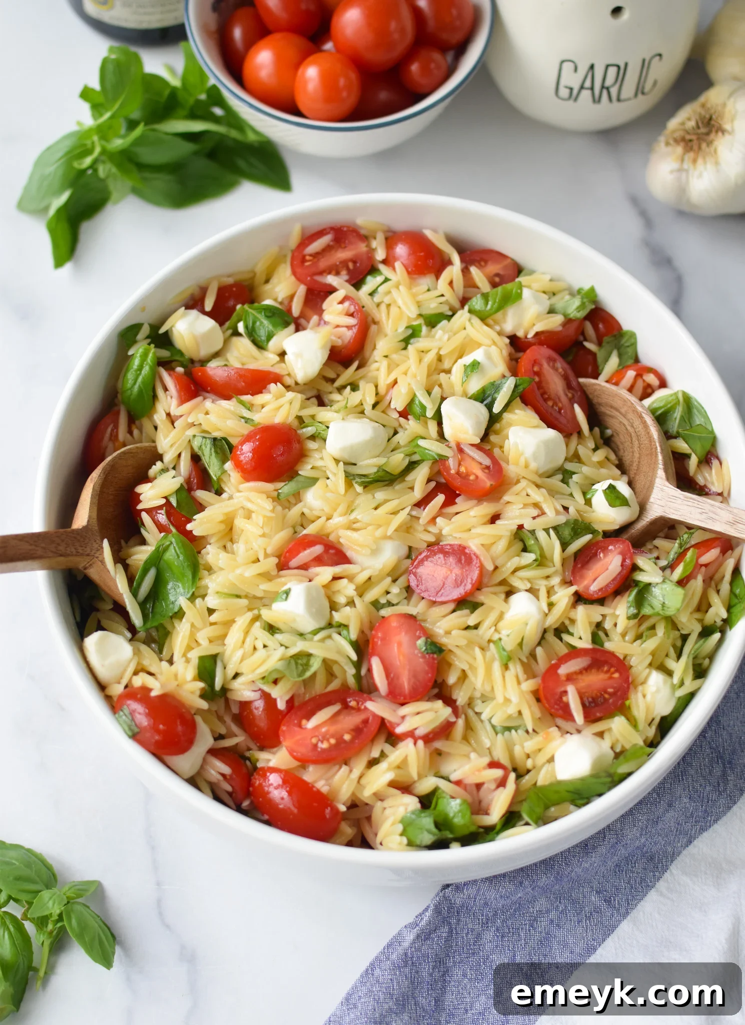 Caprese Orzo Delight 10 Caprese Orzo Pasta Salad being served with wooden spoons, highlighting freshness.
