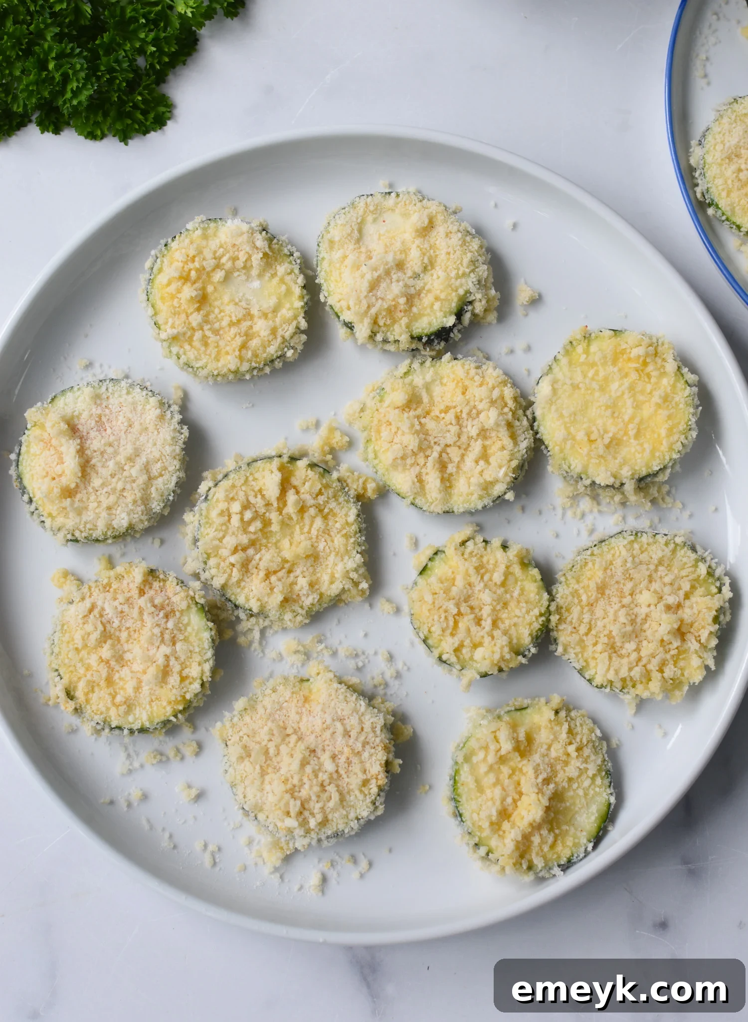 A plate of breaded zucchini chips, perfectly coated and ready to be placed into the air fryer basket.