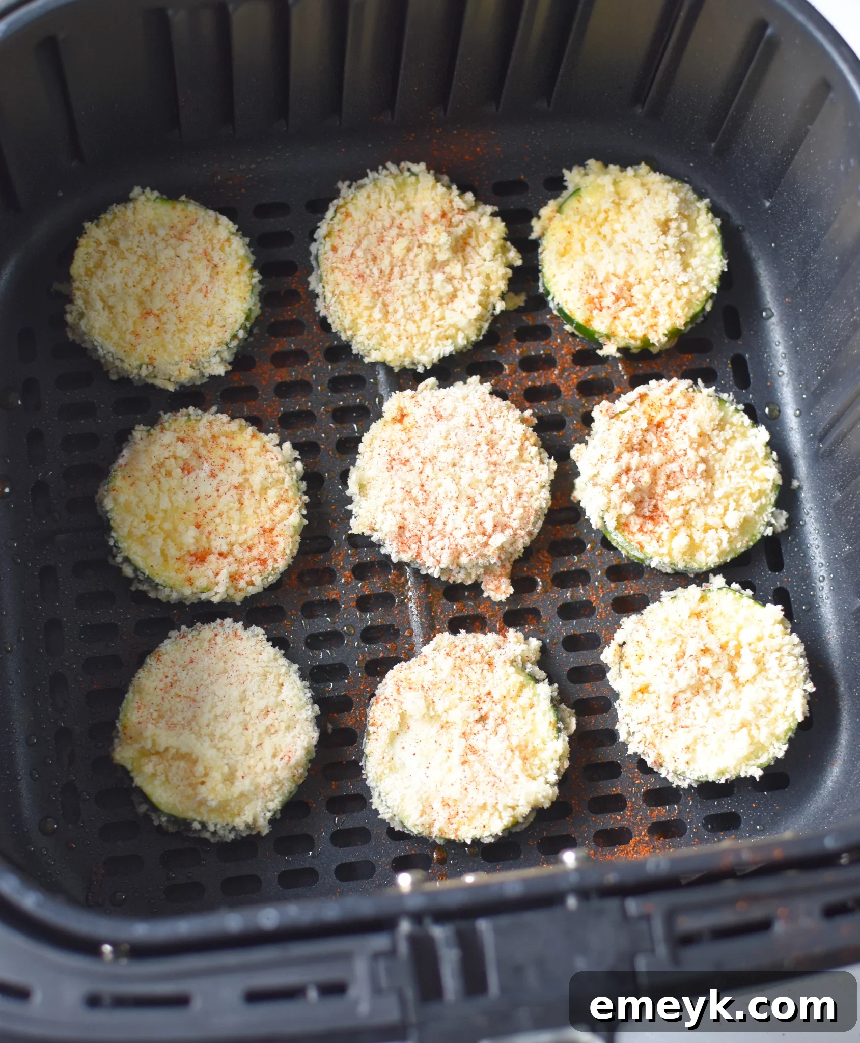 Air Fryer Zucchini chips being cooked inside an air fryer basket, showing their developing golden-brown crust.