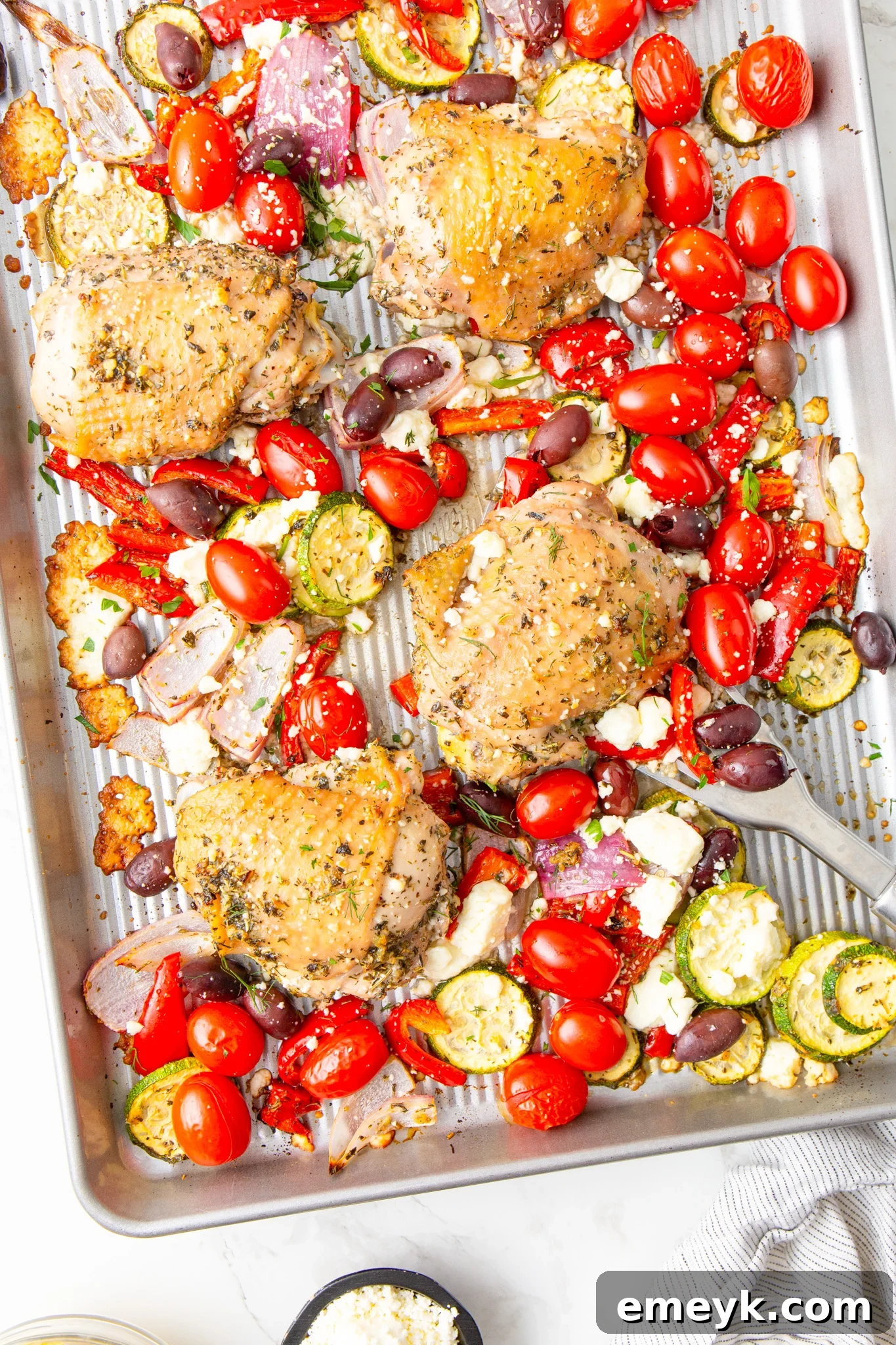 Mediterranean Sheet Pan Chicken serving with a spoon, highlighting the roasted chicken and vegetables.