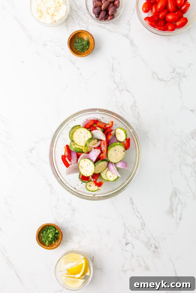 Mediterranean Sheet Pan Chicken vegetables being coated in marinade in a bowl.