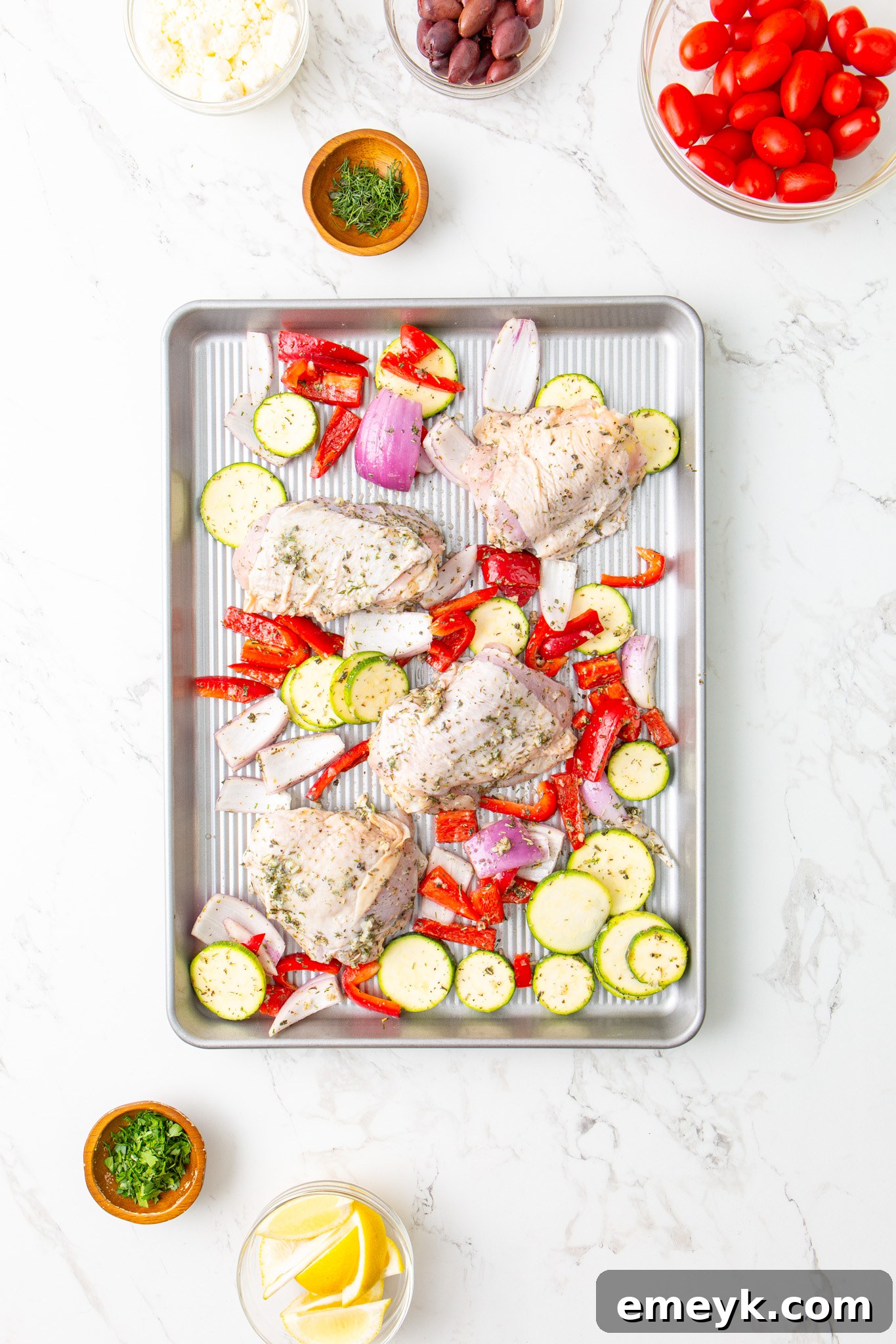 Mediterranean Sheet Pan Chicken arranged on a baking sheet before cooking, showing even distribution.