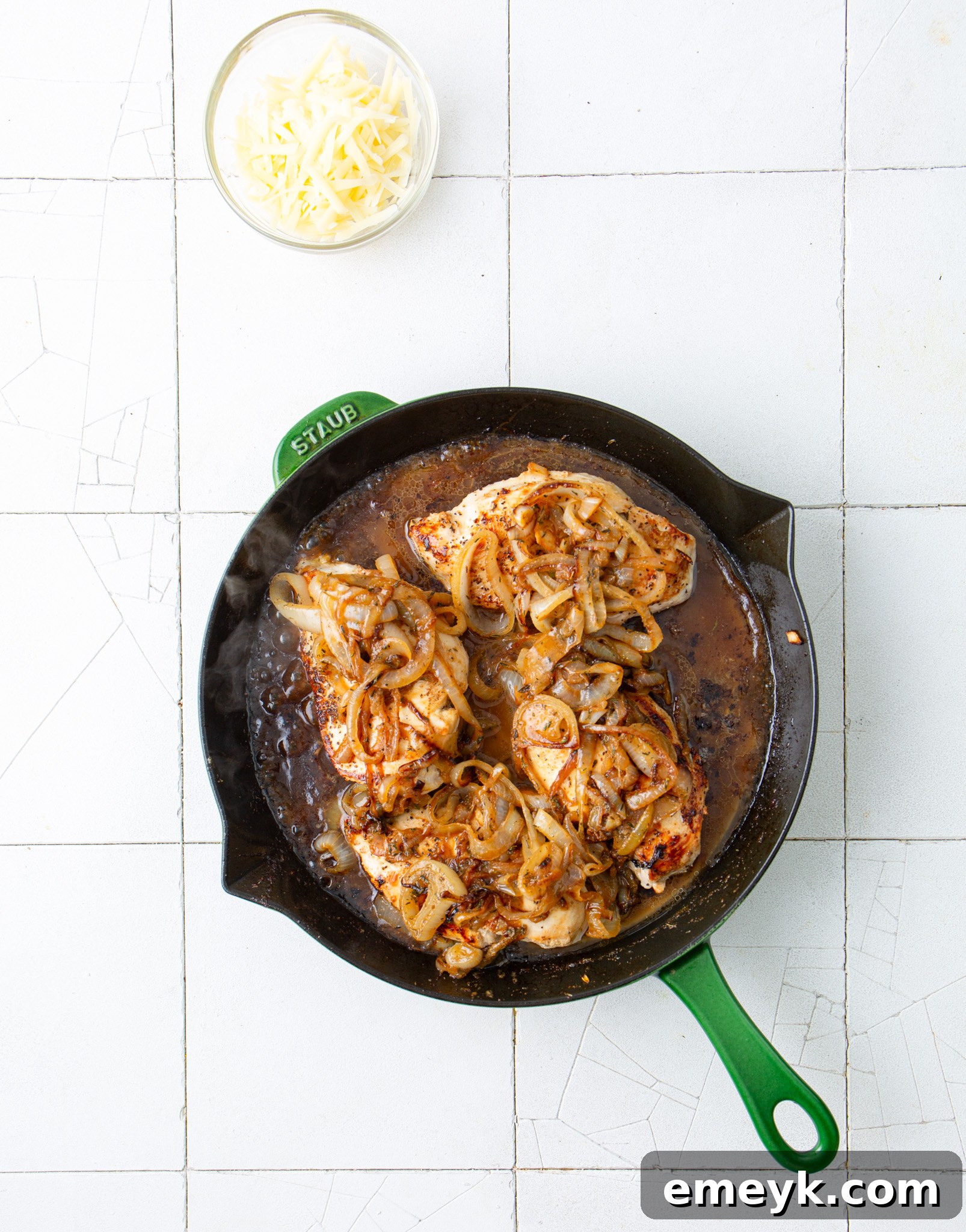 Chicken in a skillet with the sauce being added for French Onion Chicken.