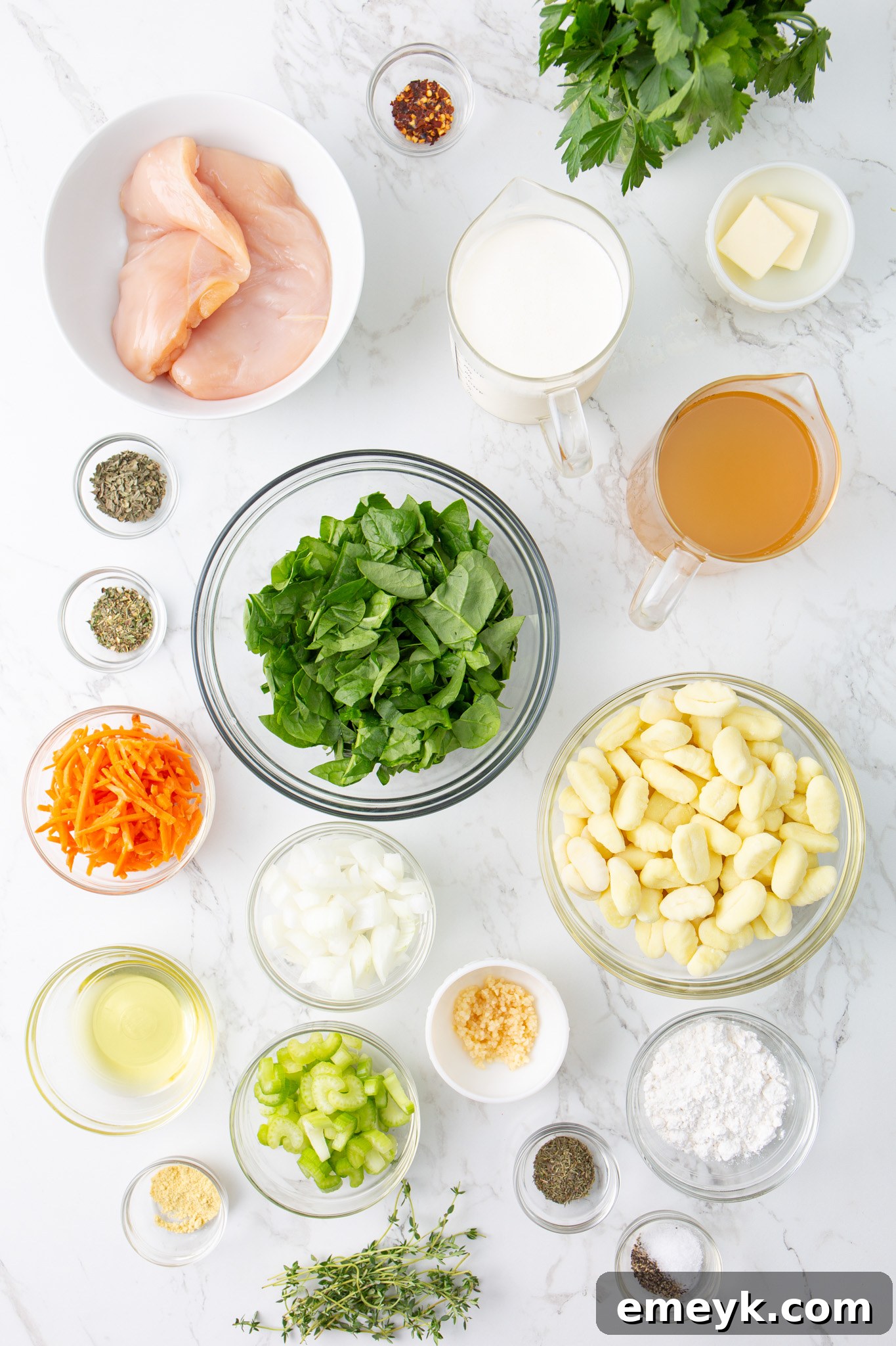 A collection of fresh ingredients laid out for the Copycat Olive Garden Chicken Gnocchi Soup, including carrots, celery, onion, garlic, chicken, gnocchi, and herbs.