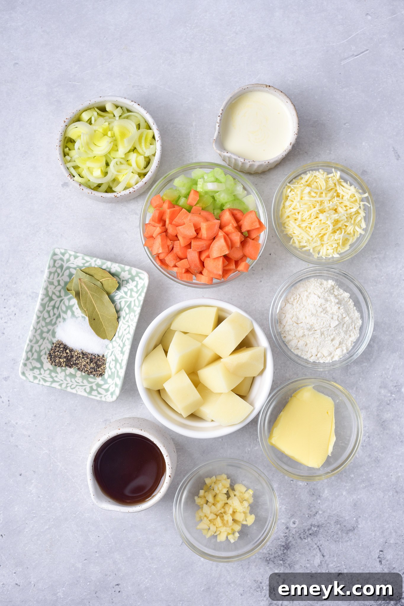 A flat lay of fresh ingredients for Creamy Potato Leek Soup, including potatoes, leeks, carrots, celery, and garlic.