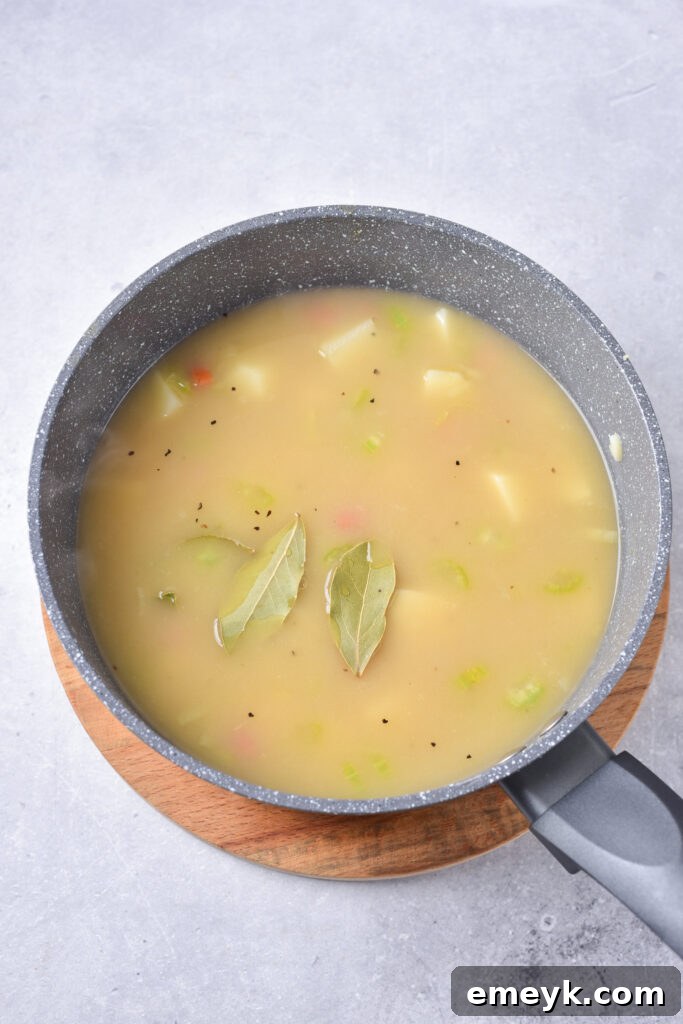 Potato Leek Soup simmering in a pot with a bay leaf, showcasing the cooking process.