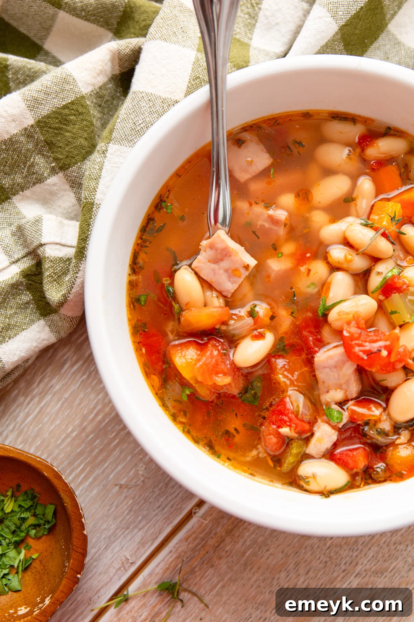 A bowl of creamy Navy Bean Soup with a spoon, garnished with fresh parsley, beside a patterned napkin.