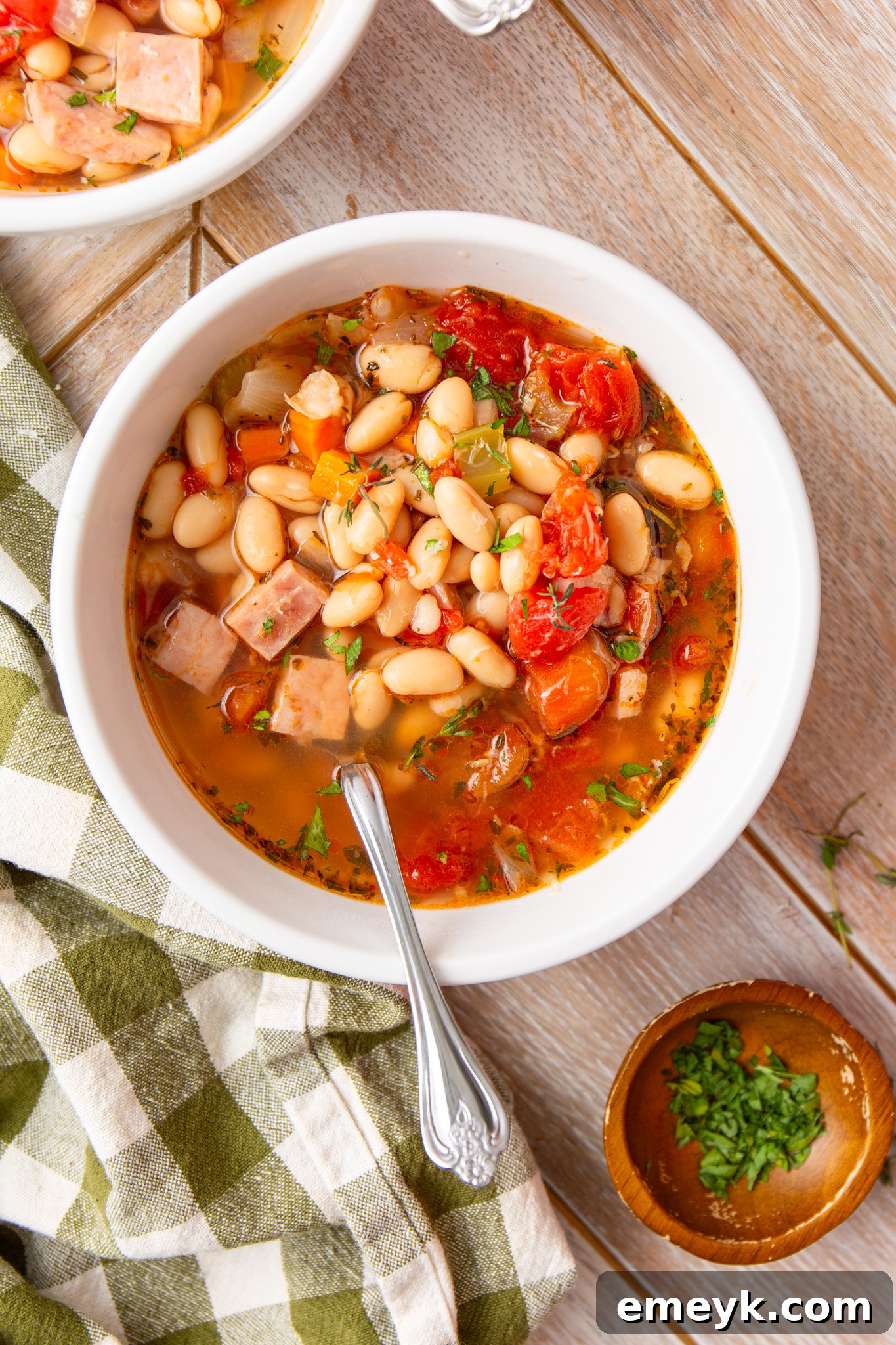 A white bowl of Navy Bean Soup garnished with fresh herbs and a spoon resting in it.
