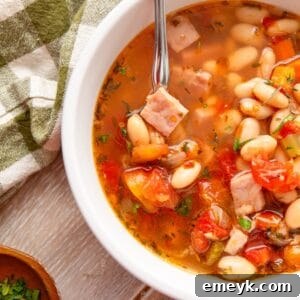 A top-down view of a hearty bowl of Navy Bean Soup with a rustic spoon.