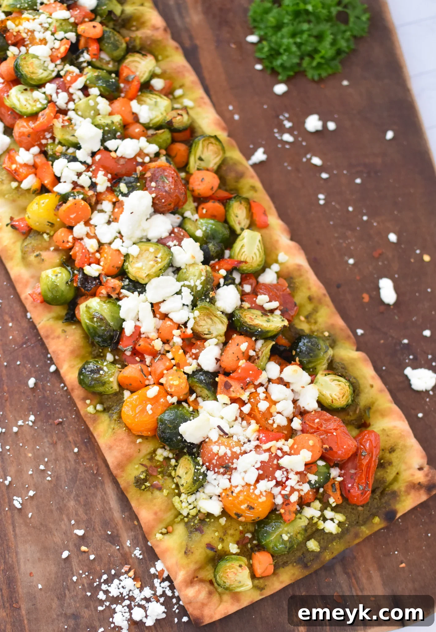 Flatbread pizzas topped with roasted vegetables and crumbled goat cheese, ready for final baking.