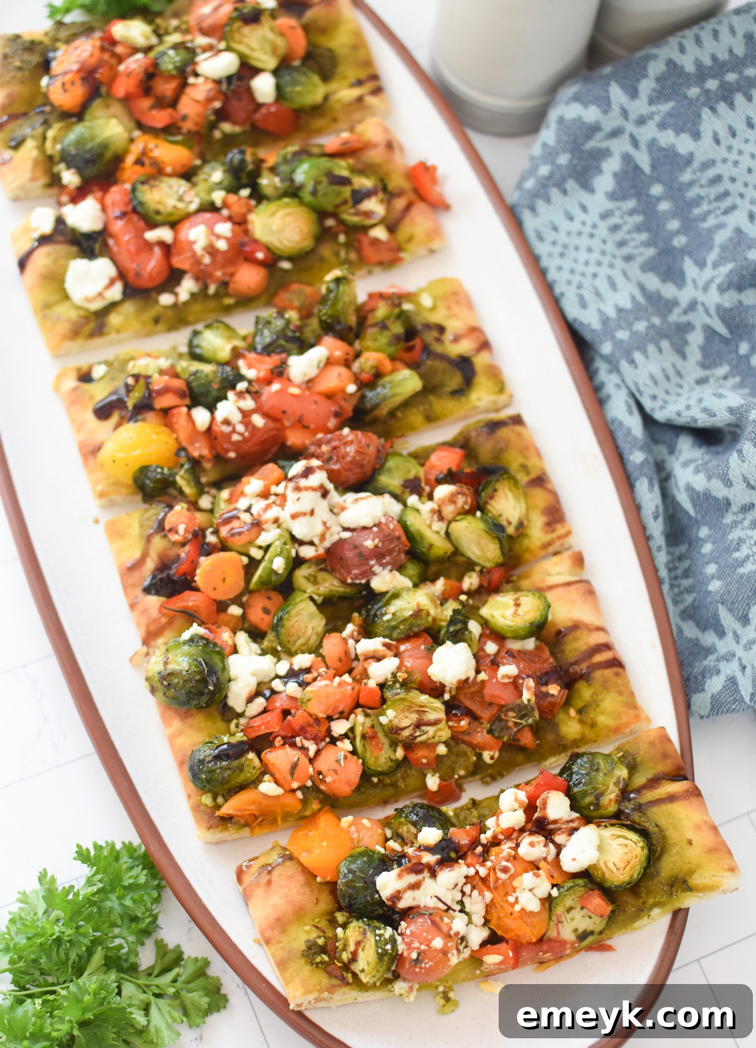 Freshly baked Roasted Vegetable Goat Cheese Flatbread Pizza, cut into slices and garnished with herbs and balsamic glaze.