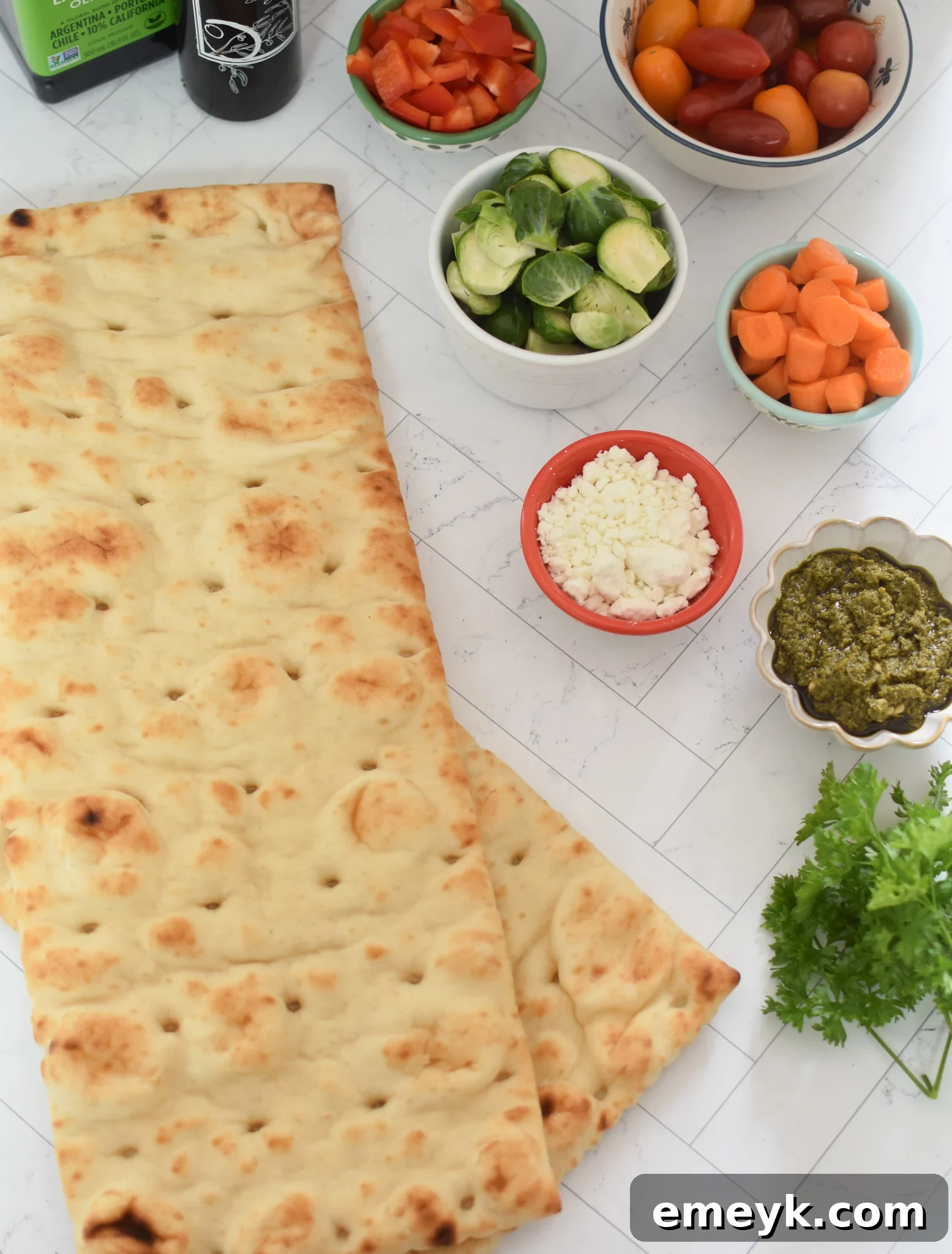 Close-up of fresh ingredients for Roasted Vegetable Goat Cheese Flatbread Pizza, including various vegetables, goat cheese, and pesto.
