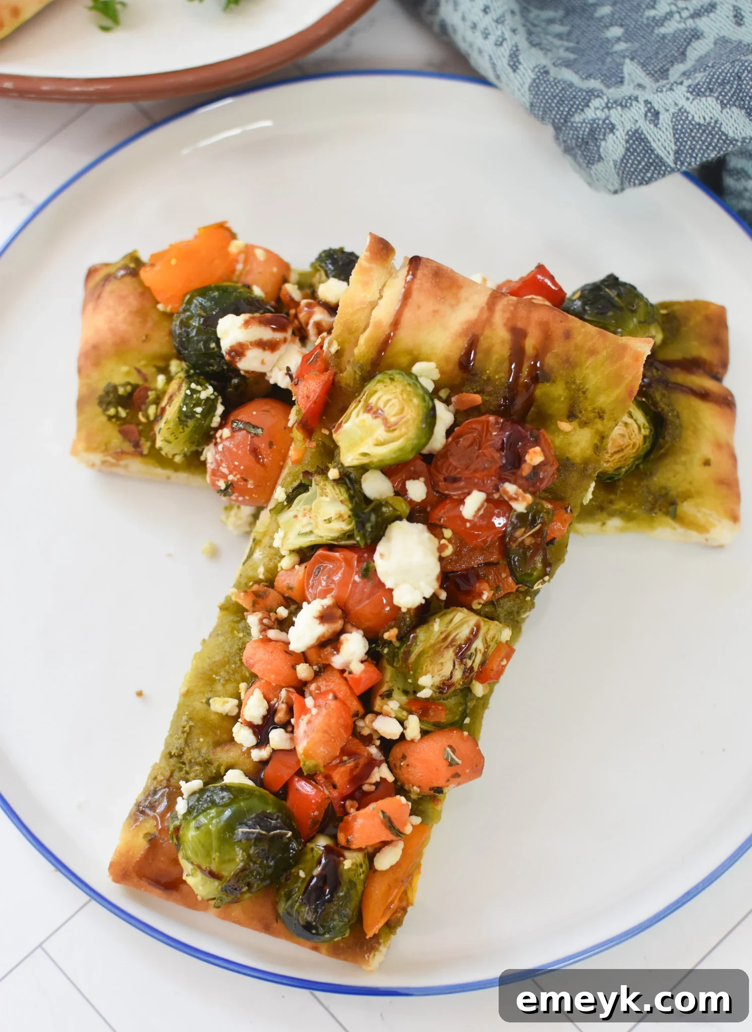 A slice of Roasted Vegetable Goat Cheese Flatbread Pizza on a white plate, garnished with fresh herbs.