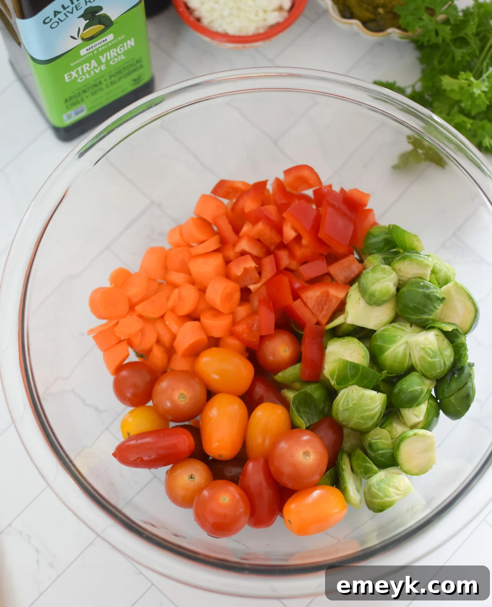 Mixed bell pepper, carrots, and Brussels sprouts in a bowl, coated with olive oil and ready for seasoning.