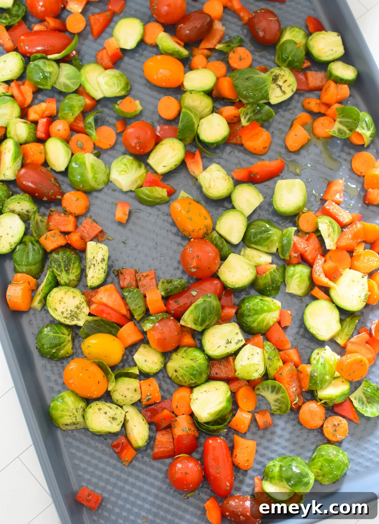 Seasoned bell pepper, carrots, and Brussels sprouts spread on a baking sheet, ready for the oven.