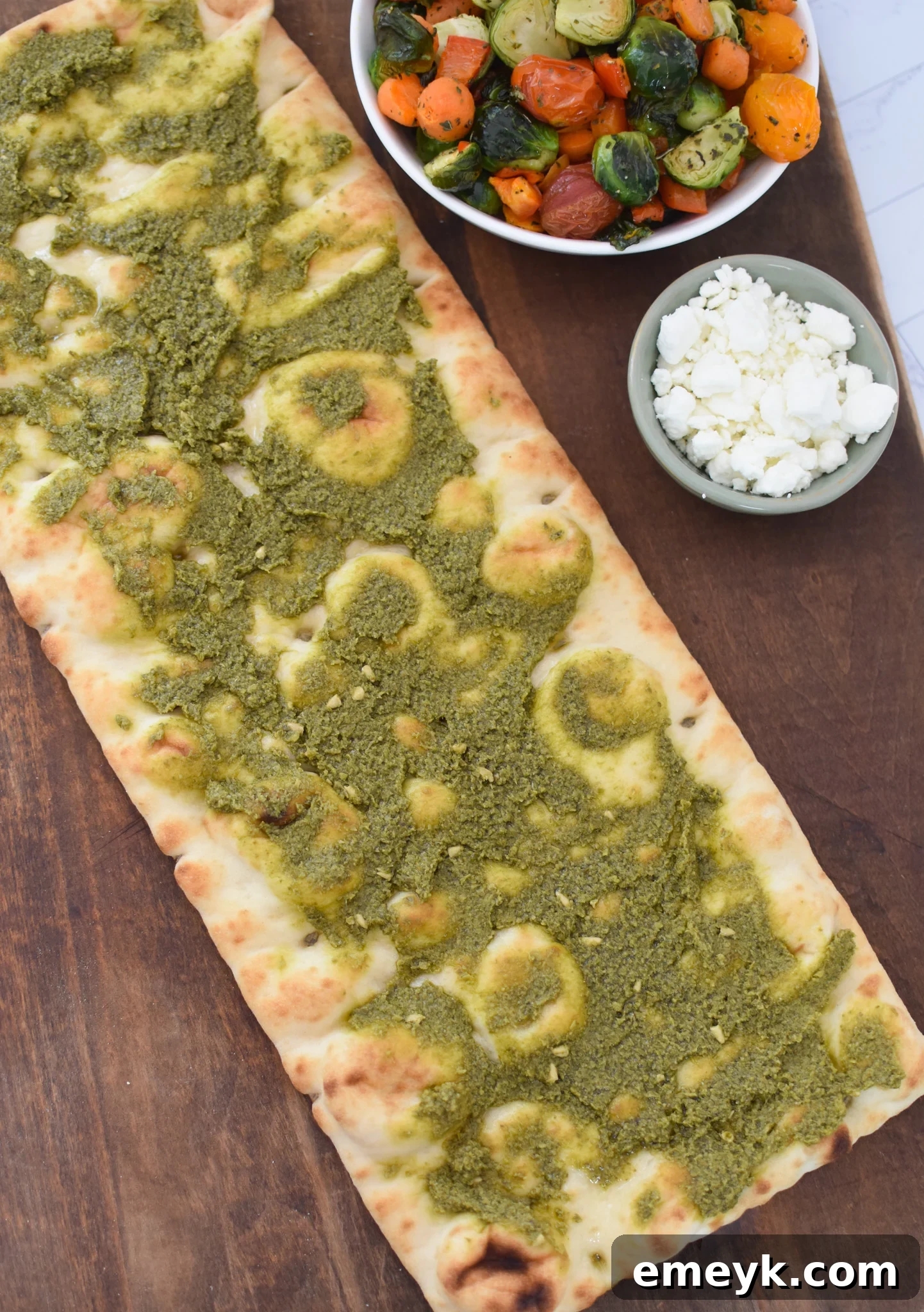 Flatbreads on a baking sheet, covered with a thin layer of vibrant green pesto.
