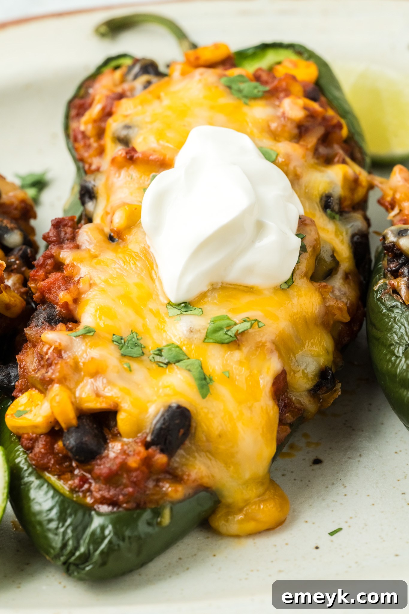 Baked Stuffed Poblano Peppers arranged on a baking sheet, fresh from the oven, with a dollop of sour cream on top of one pepper.