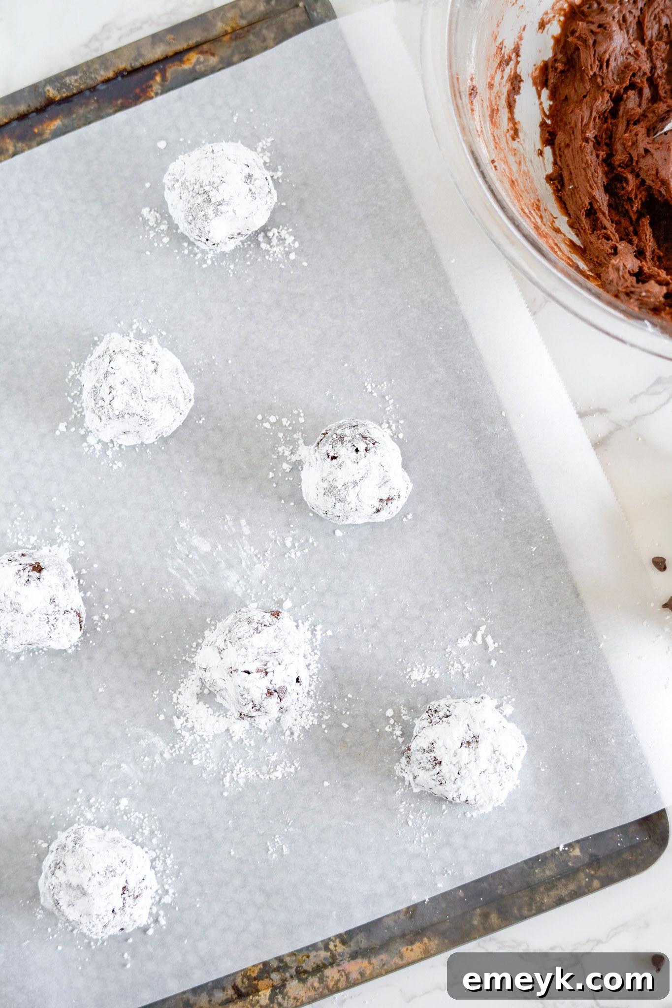 Chocolate Crinkle Cookie dough balls arranged on a parchment-lined baking sheet, ready for the oven.