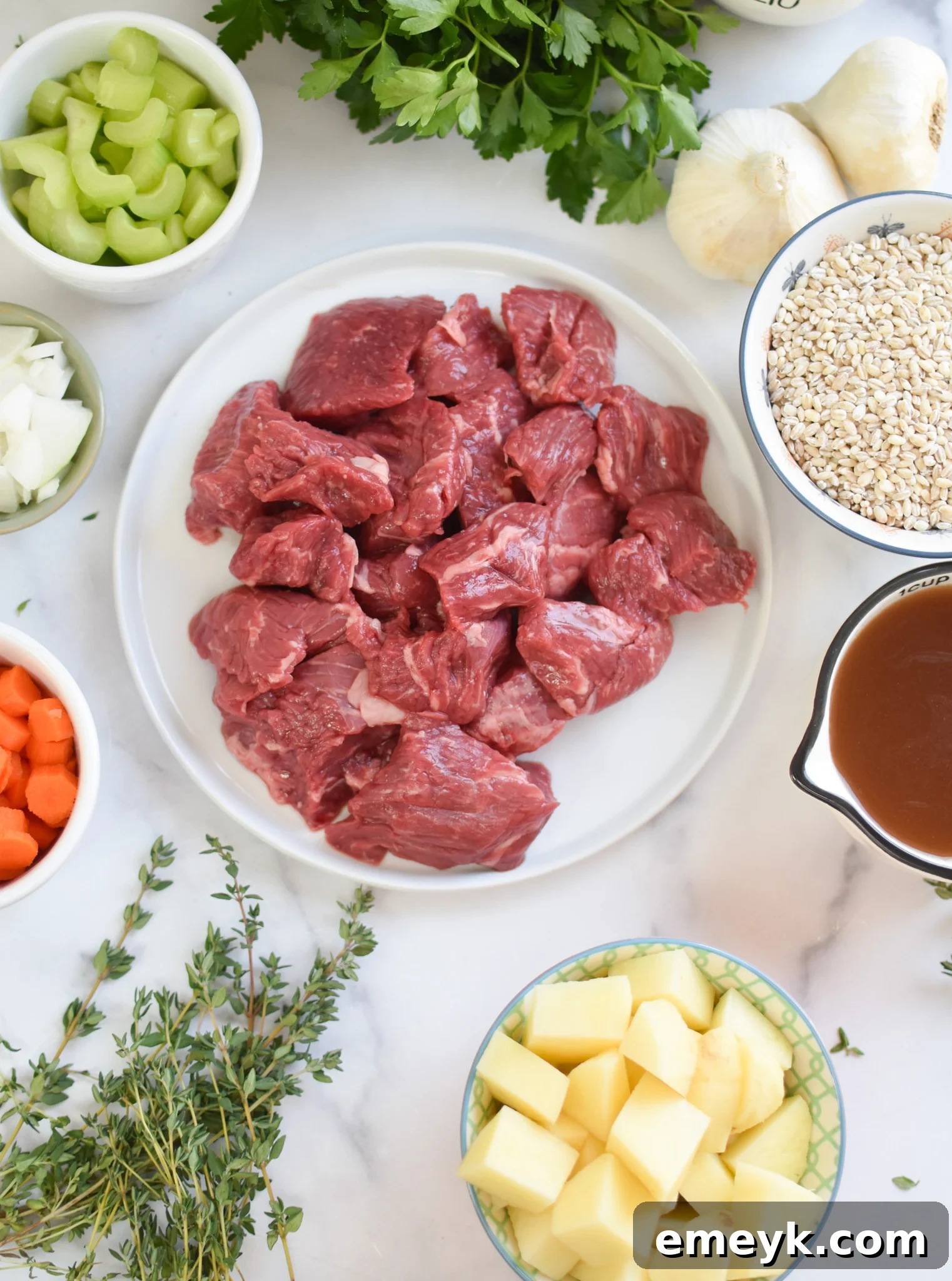 A vibrant flat lay of all the fresh ingredients needed for Slow Cooker Beef Barley Soup, including chuck roast, vegetables, potatoes, and spices.