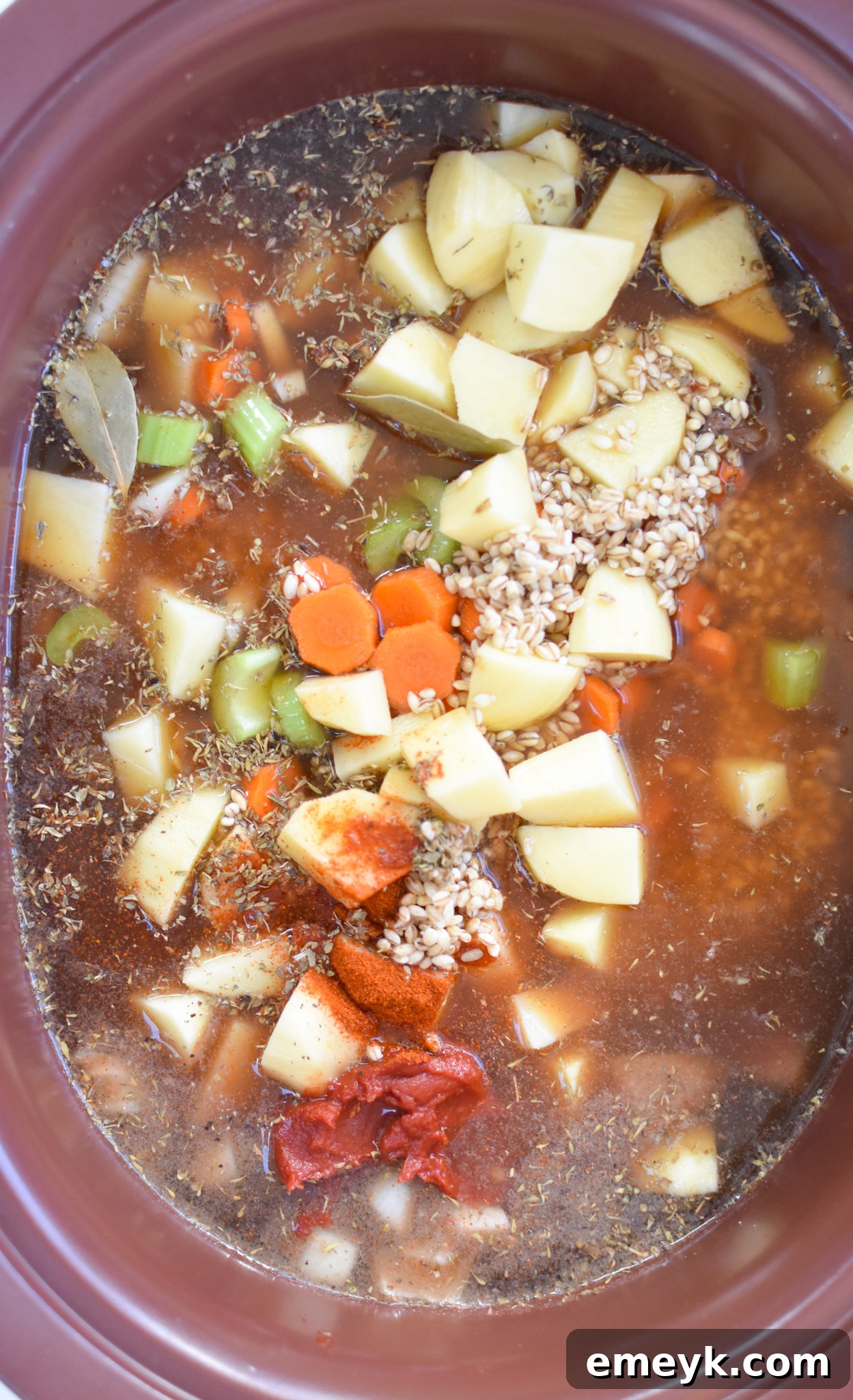 All the raw ingredients for Slow Cooker Beef Barley Soup, including beef, vegetables, potatoes, and barley, gathered in a crockpot before cooking.