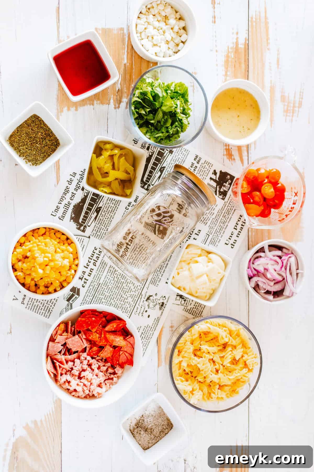 A flat lay shot showcasing all the fresh ingredients for an Italian Pasta Mason Jar Salad, including pasta, vegetables, meats, cheese, and dressing components.