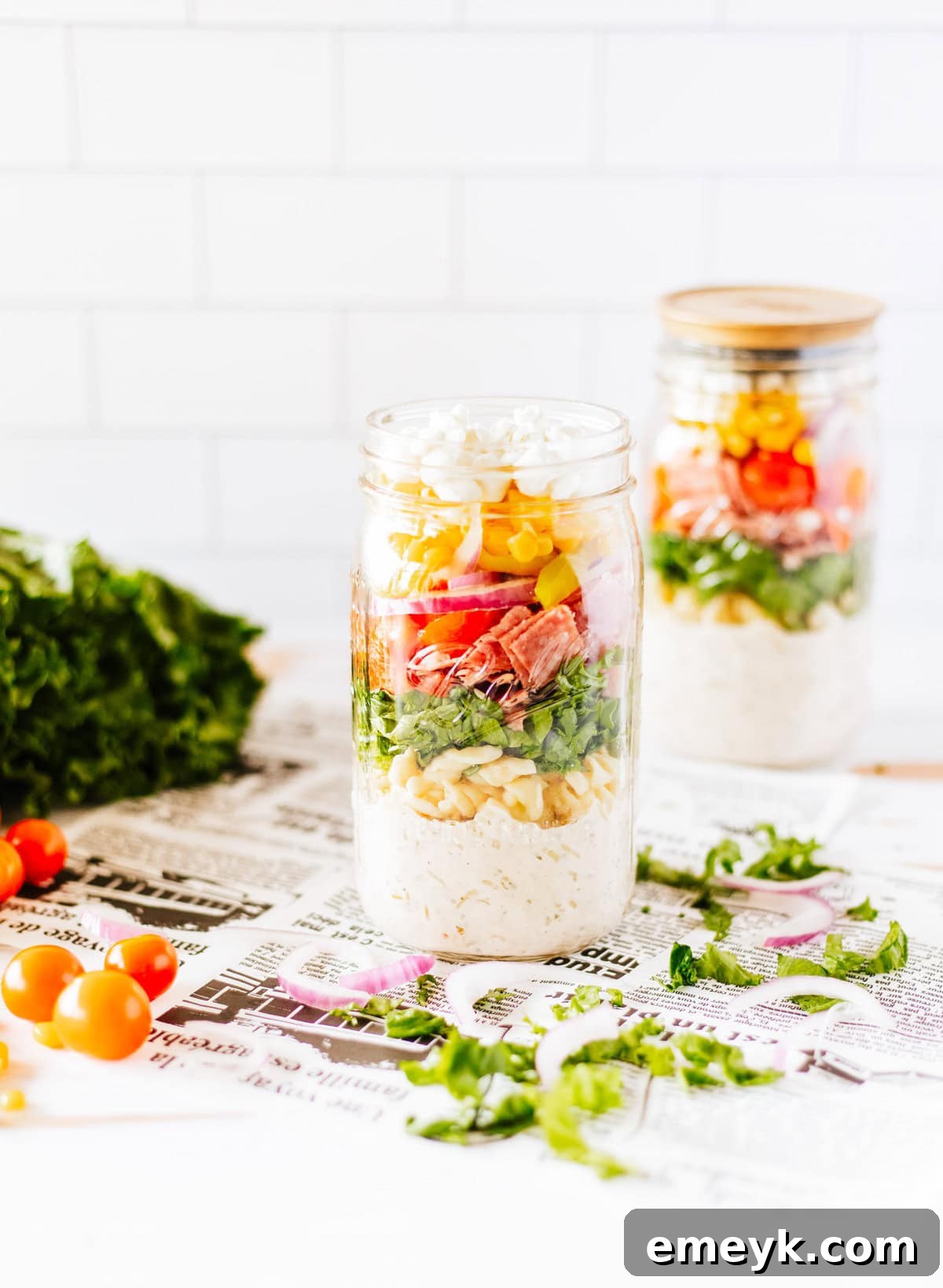 Two Italian Pasta Mason Jar Salads side-by-side, showcasing their appealing layers and readiness for meal prep, with a spoon nearby.