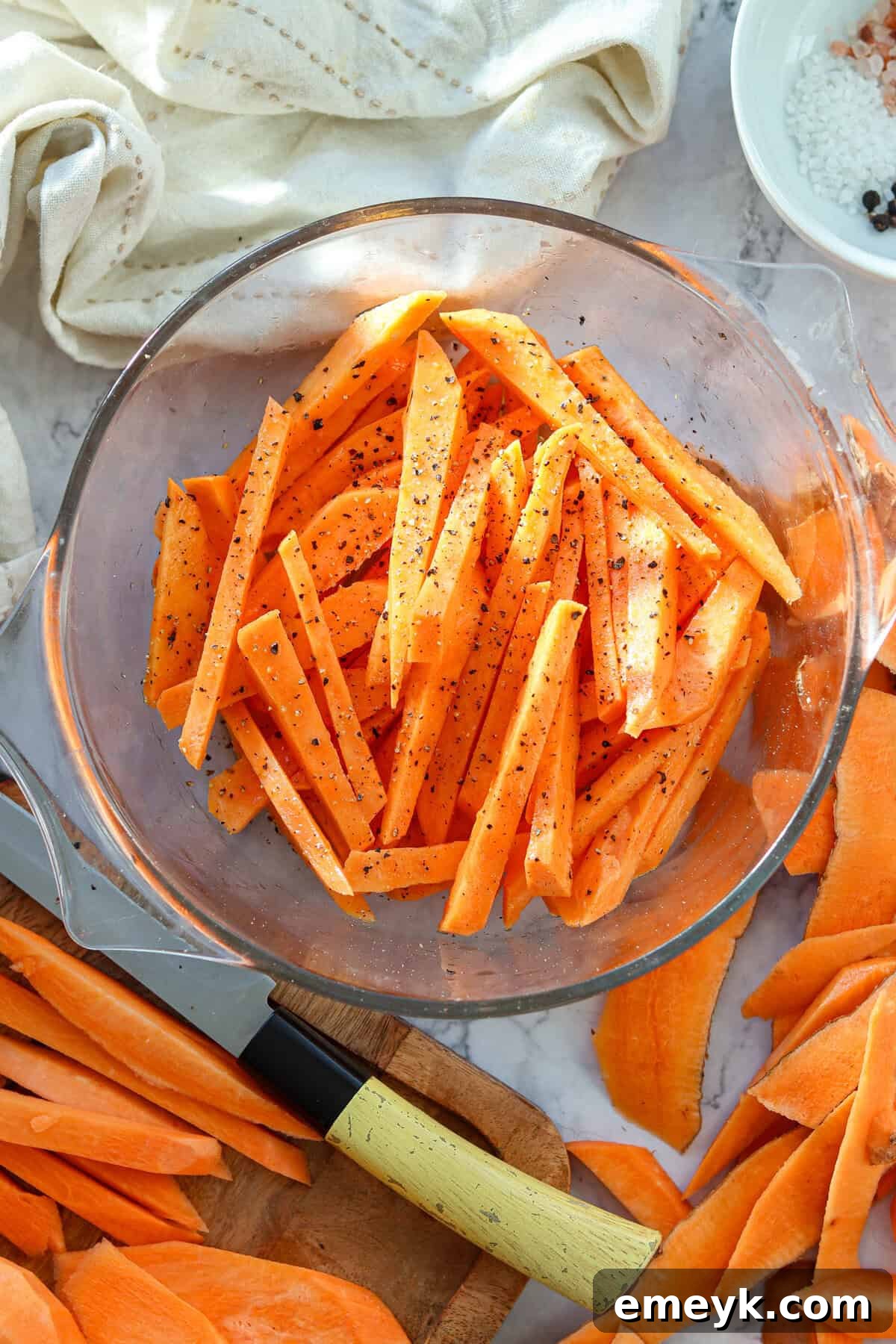 Sweet potato fries tossed with olive oil and spices in a mixing bowl