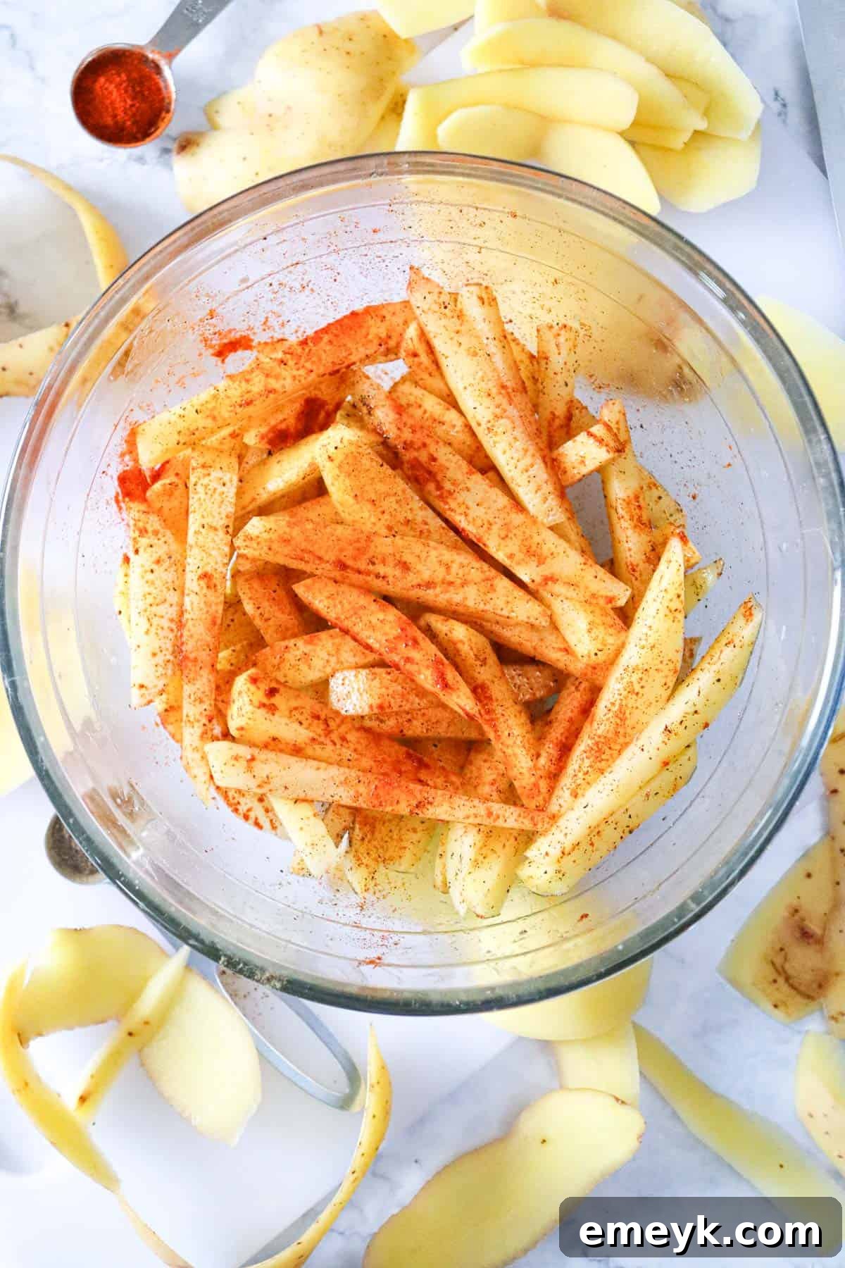 Potato fries being tossed with olive oil and a blend of spices in a mixing bowl