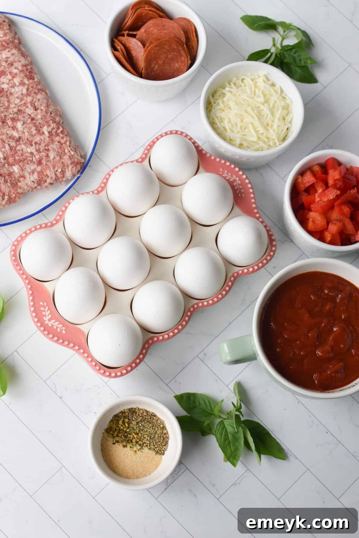 A vibrant display of fresh ingredients for Pizza Egg Muffins, including eggs, bell pepper, sausage, pepperoni, cheese, and herbs