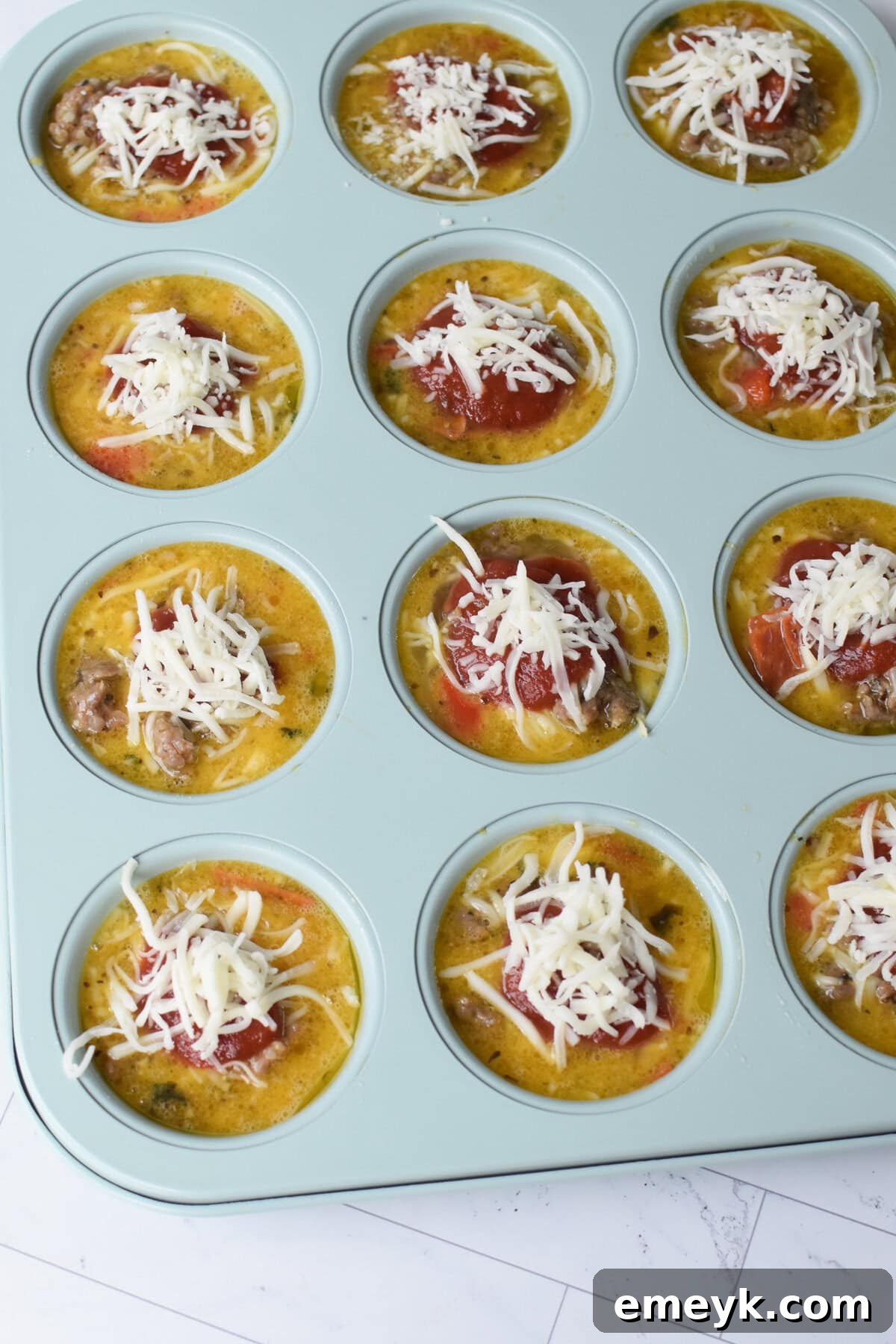Unbaked Pizza Egg Muffins filled with egg mixture, topped with pizza sauce and cheese, ready for the oven