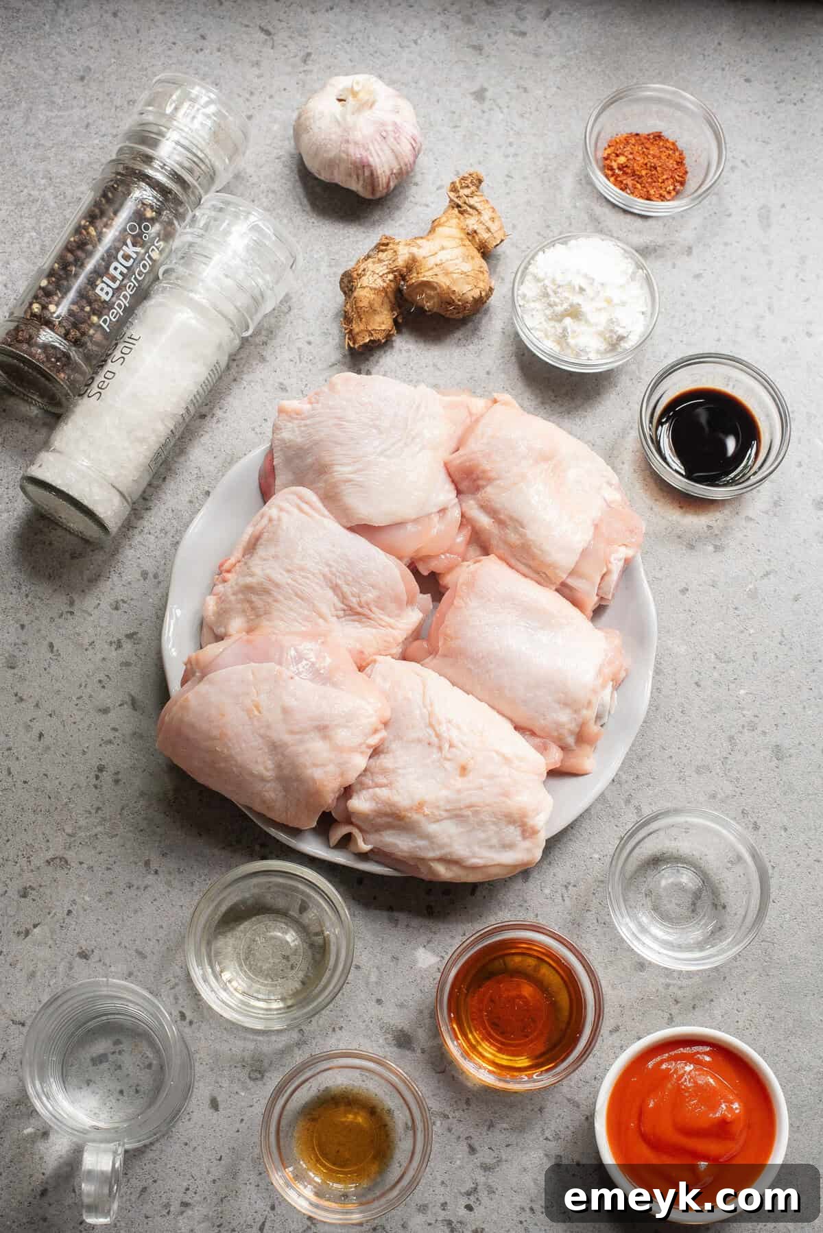 Array of fresh ingredients including chicken thighs, ginger, garlic, honey, soy sauce, and sriracha.
