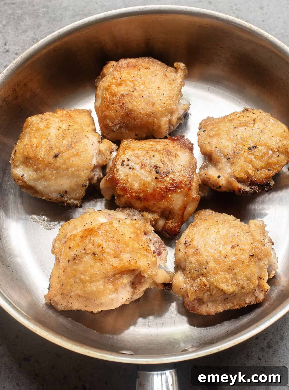 Chicken thighs searing in a hot skillet, developing a golden crust.