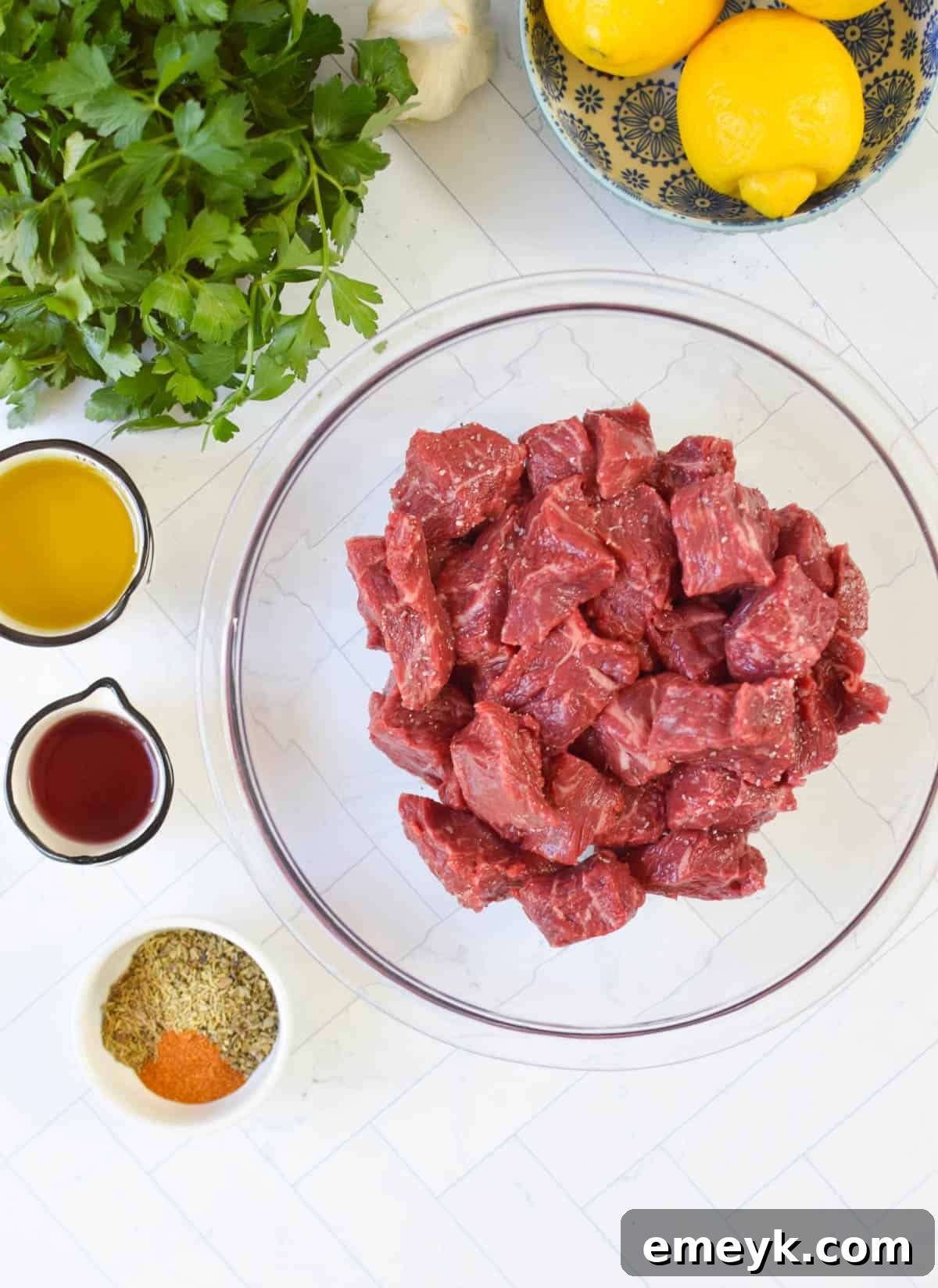 Various Beef Souvlaki ingredients, including cubed beef, fresh vegetables, and marinade components, laid out on a wooden surface.