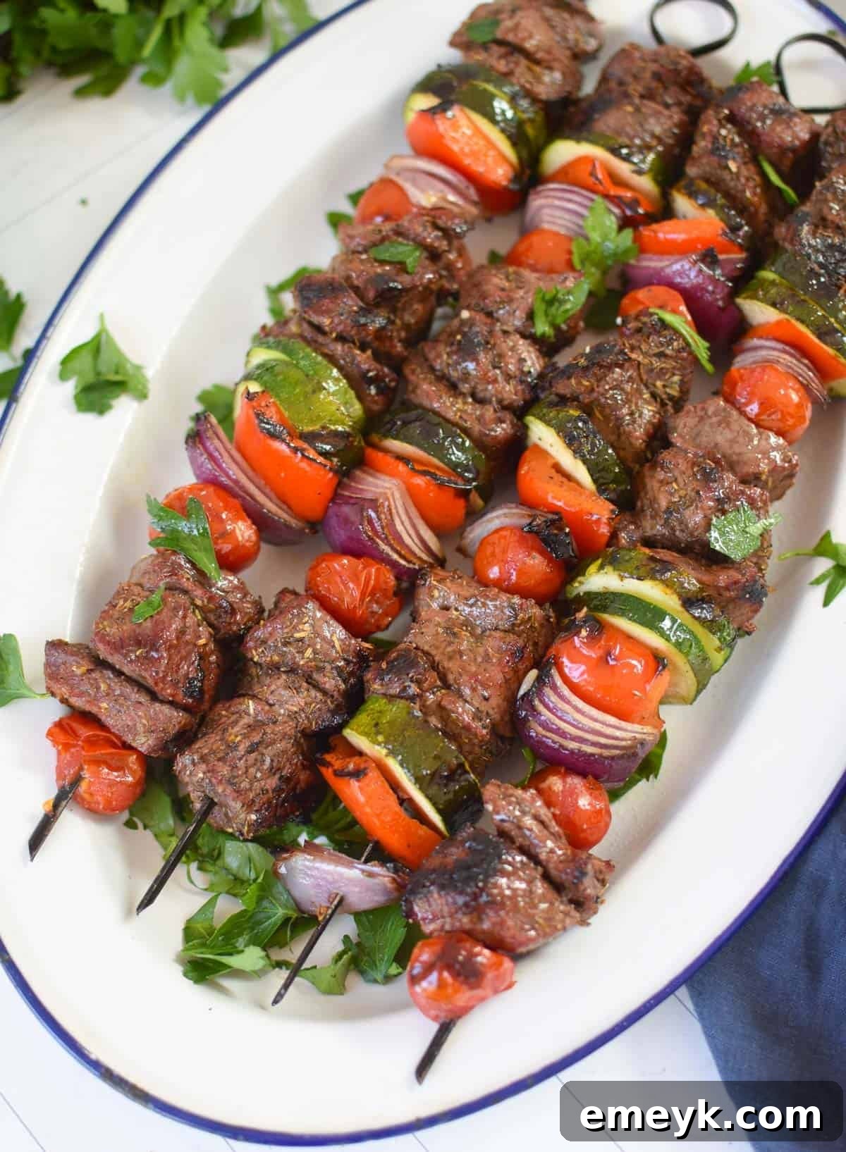 Grilled Beef Souvlaki skewers presented on a clean white platter with fresh herbs, ready for serving.