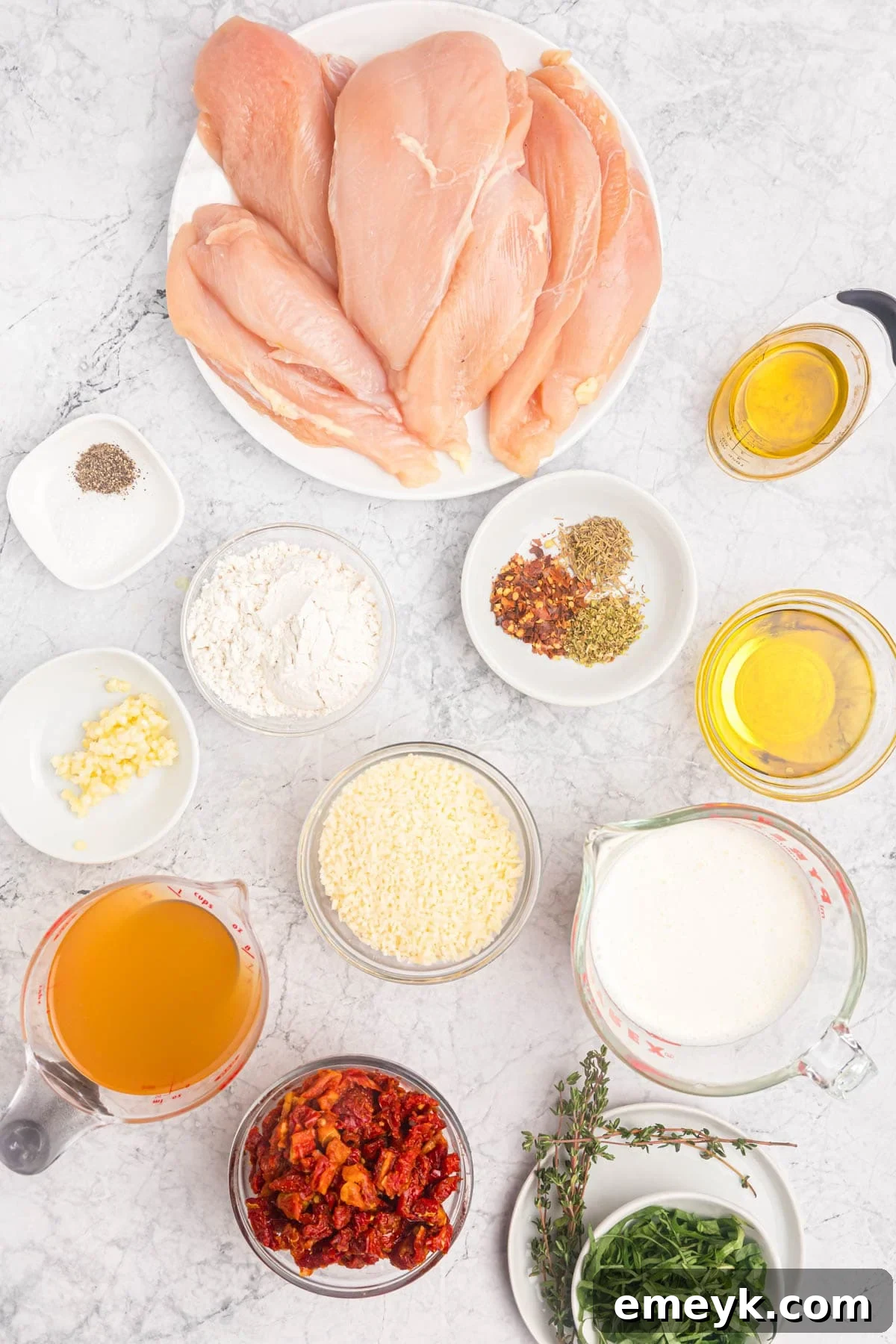 A flat lay photograph showcasing all the fresh ingredients for Marry Me Chicken, including chicken breasts, sun-dried tomatoes, garlic, cream, and herbs.