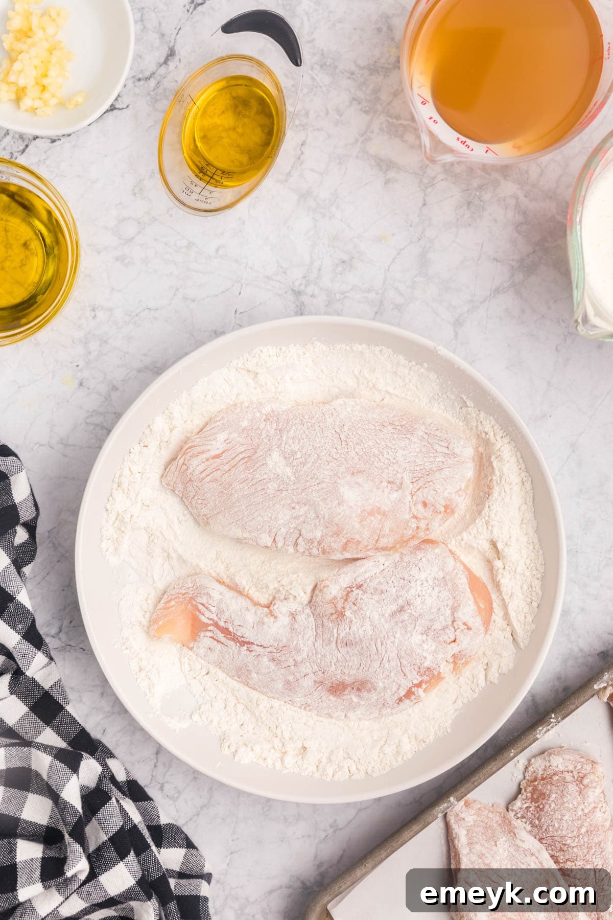 Chicken cutlets being dredged in flour, ready for browning in the Marry Me Chicken recipe.