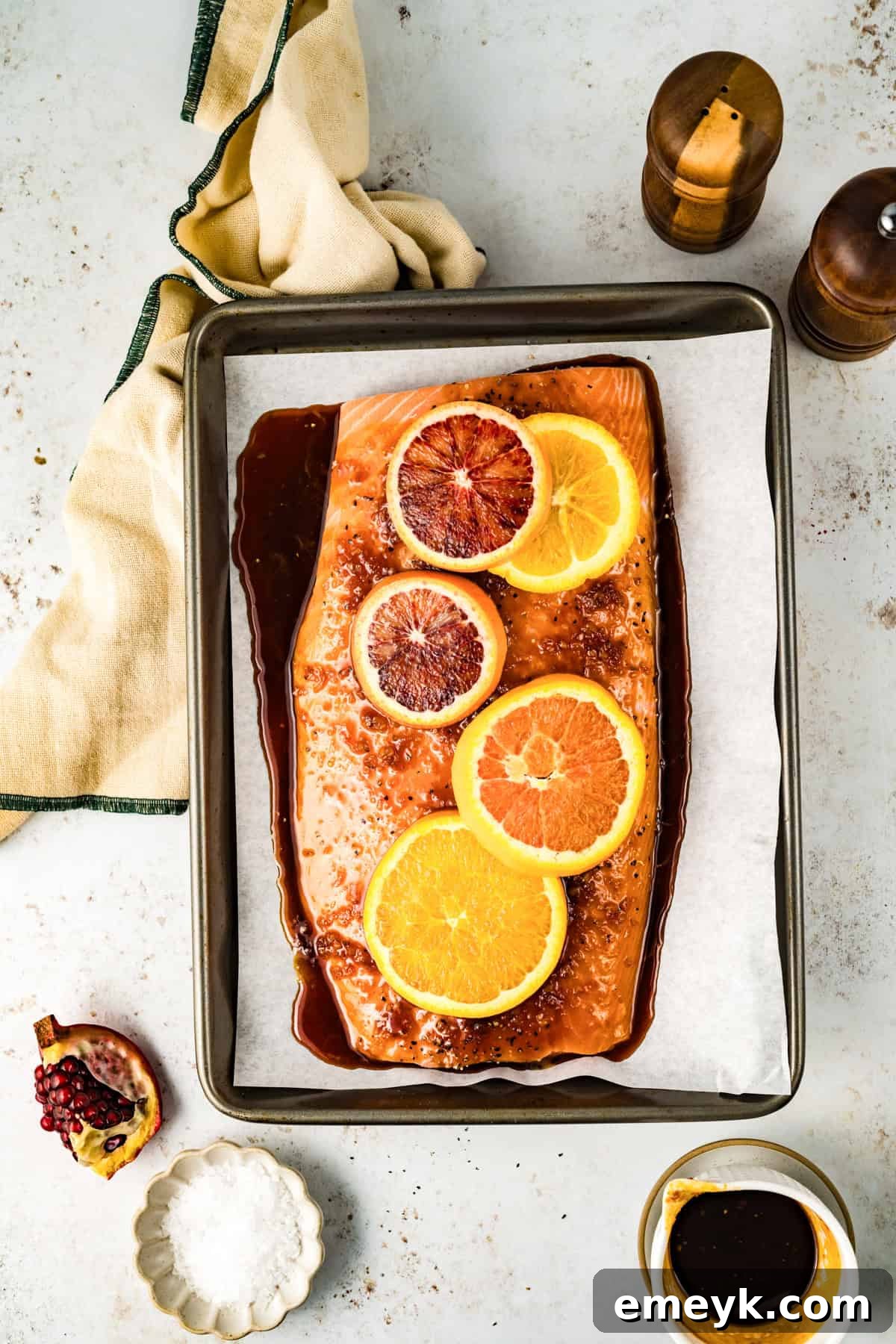 Raw salmon fillets on a baking sheet, generously coated with the vibrant orange glaze and adorned with fresh orange slices before baking.