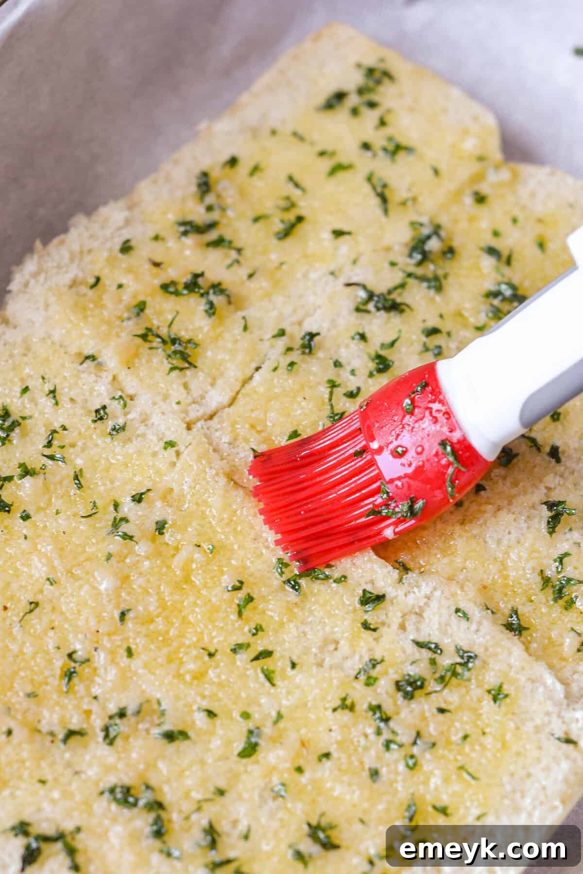 Garlic butter being brushed onto the bottom Hawaiian rolls