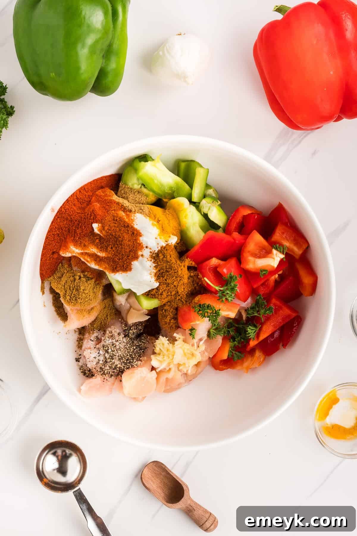 Chicken pieces and bell peppers coated in a rich, orange-hued Tikka marinade in a mixing bowl.