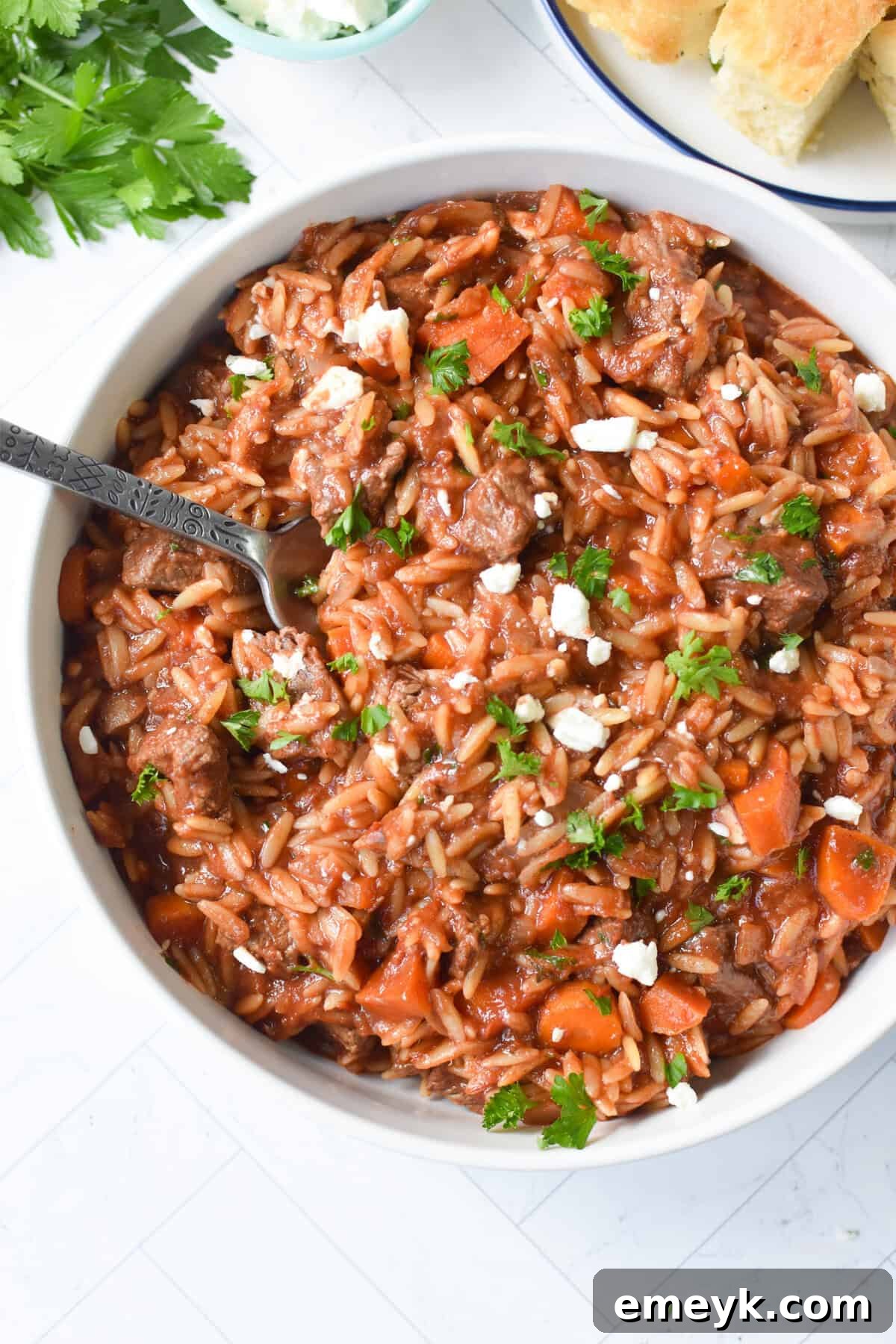 Hearty Greek Beef Stew with Orzo served in a white bowl with a spoon, garnished with fresh herbs and feta cheese.