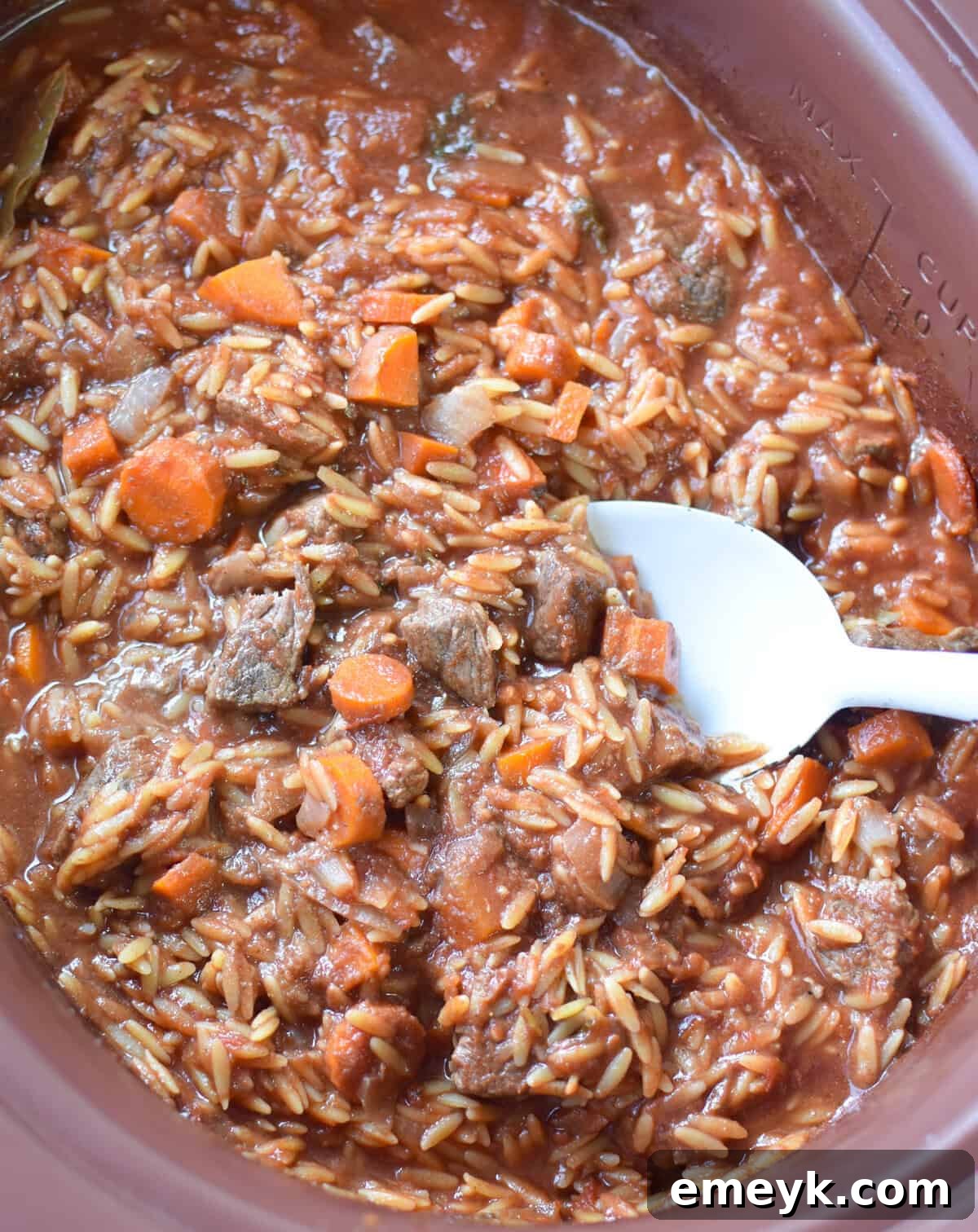 Greek Beef Stew with Orzo cooking slowly in a crockpot, showing the rich red sauce and tender meat.