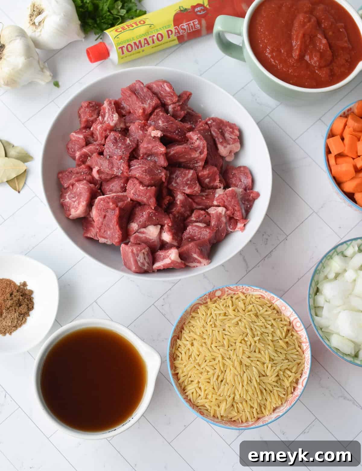 Collection of fresh ingredients for Greek Beef Stew with Orzo, including chuck roast, vegetables, spices, and pasta.
