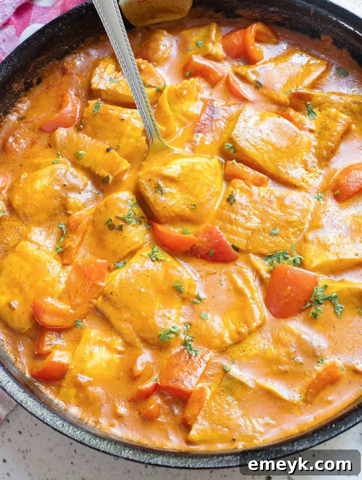 Coconut Fish Curry in a skillet with a spoon, garnished with fresh cilantro