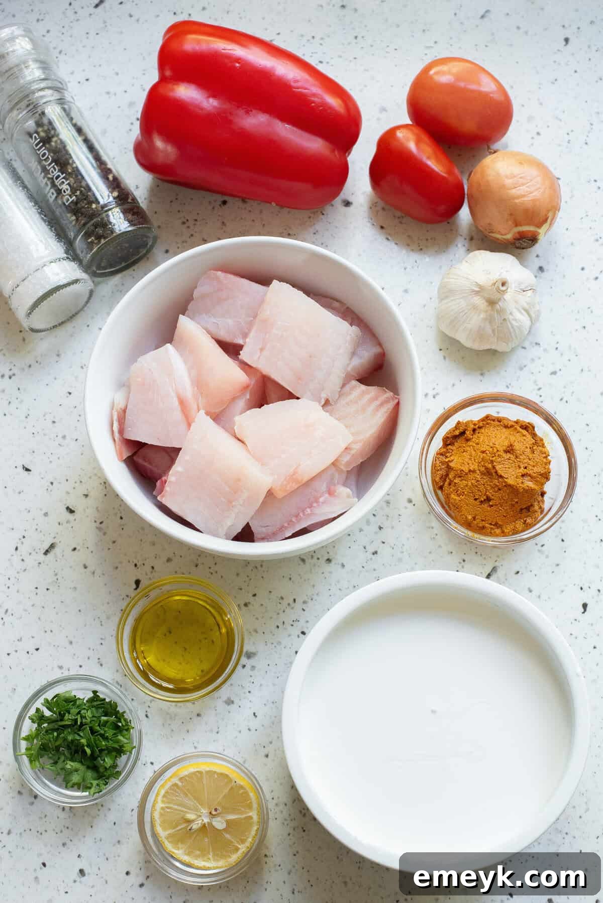 A selection of fresh ingredients laid out for Coconut Fish Curry, including fish fillets, vegetables, and spices