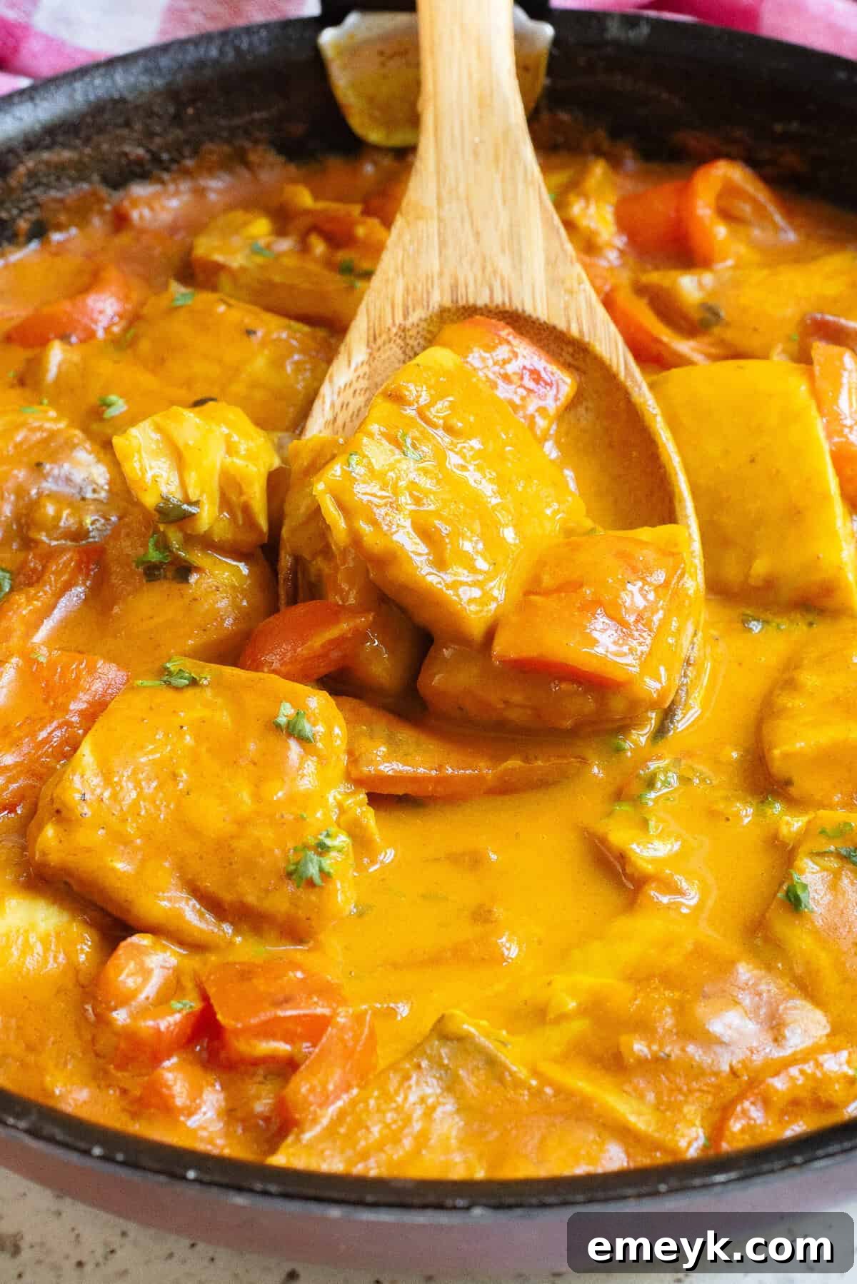 Coconut Fish Curry simmering in a skillet, with a spoon for stirring
