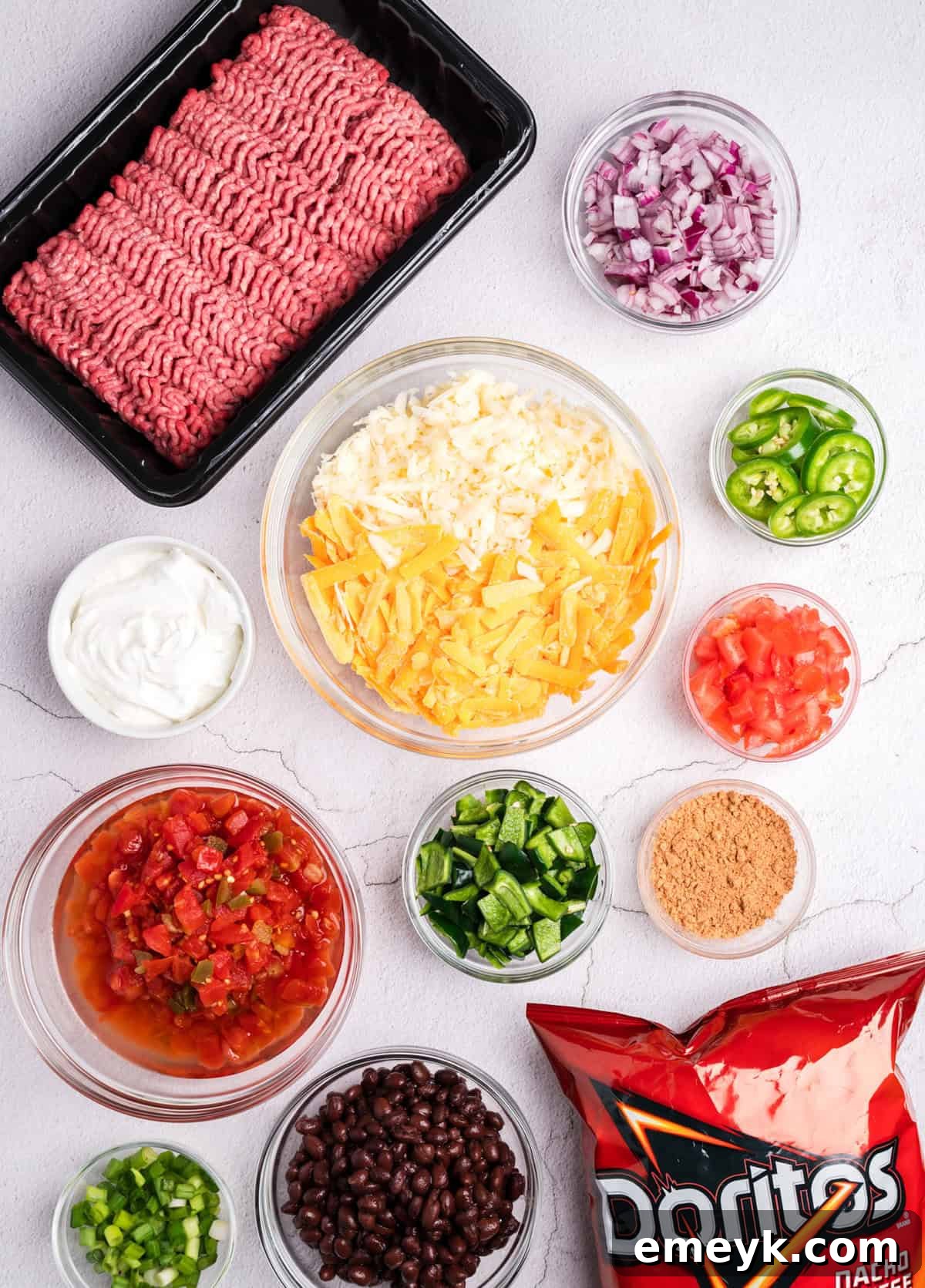 A flat lay photograph showcasing all the fresh ingredients needed for Doritos Taco Casserole, including ground beef, vegetables, cheese, and a bag of Doritos.
